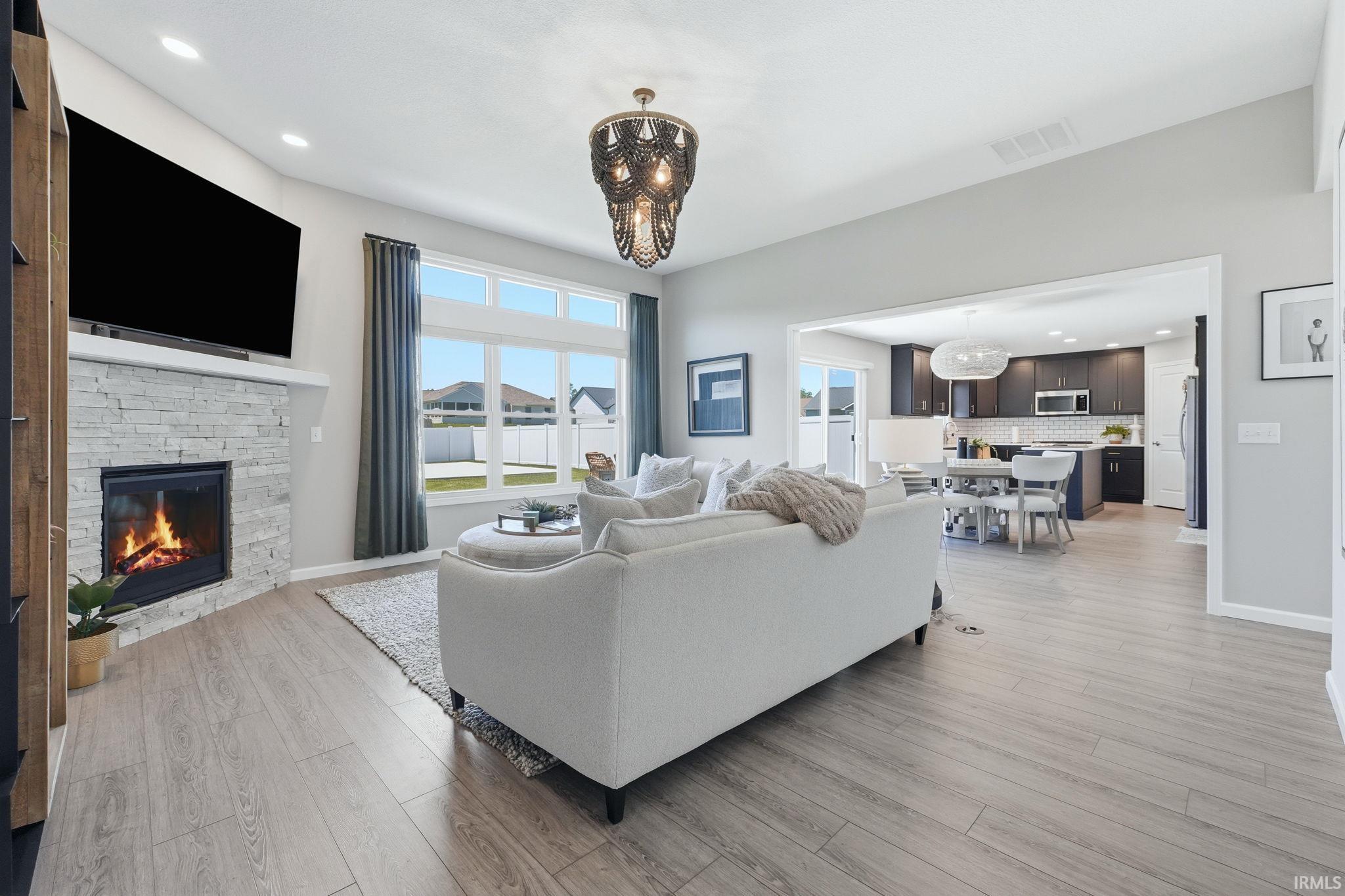 Spacious living area featuring a stacked stone fireplace with mantle, wood-finish flooring, recessed lighting, and a contemporary chandelier
