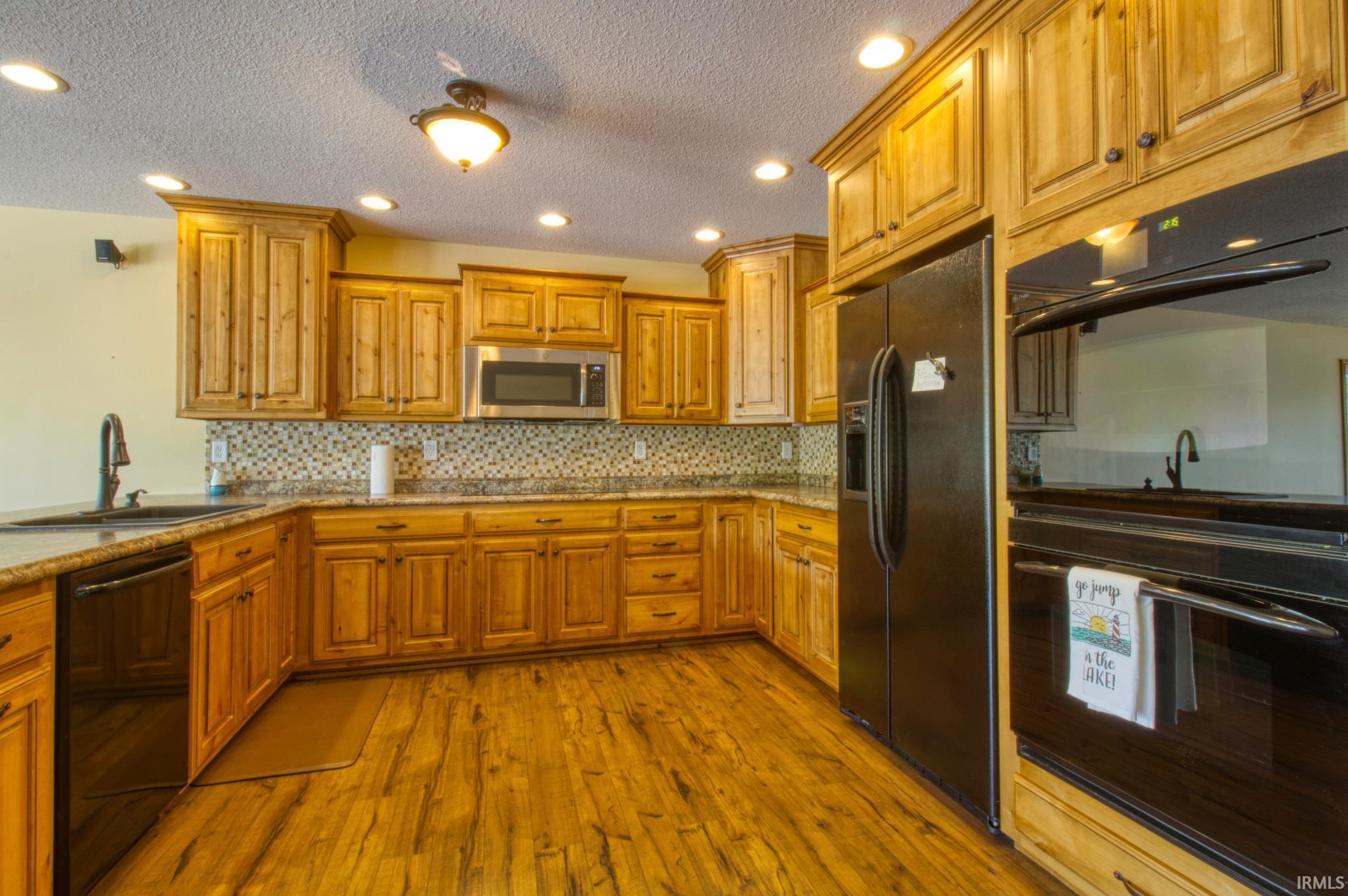 Kitchen featuring abundant wood cabinetry, wood-finish flooring, granite countertops, and a mosaic tile backsplash