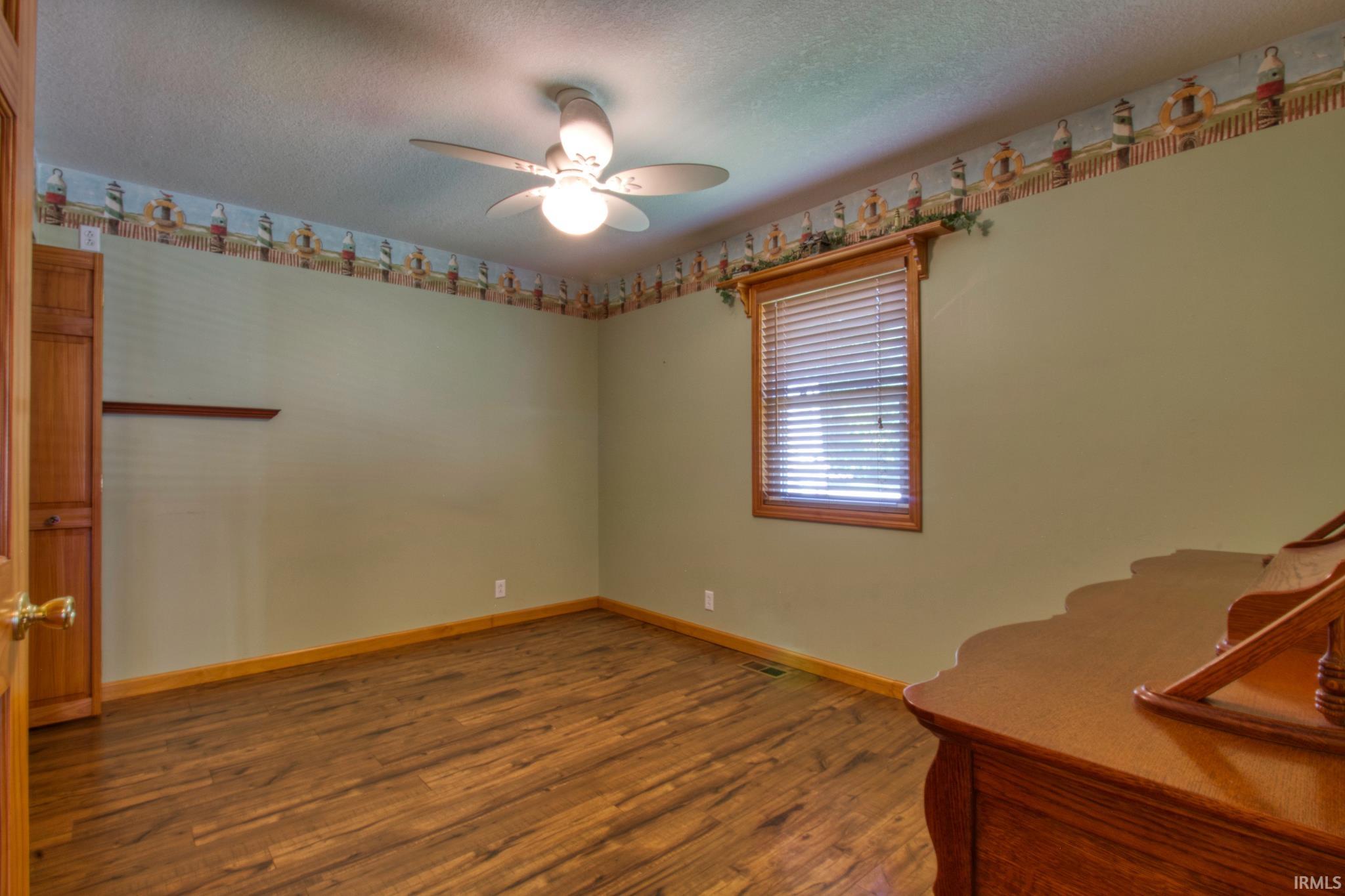 Spacious room featuring wood-finish flooring, a ceiling fan with integrated lighting, and a single window with blinds