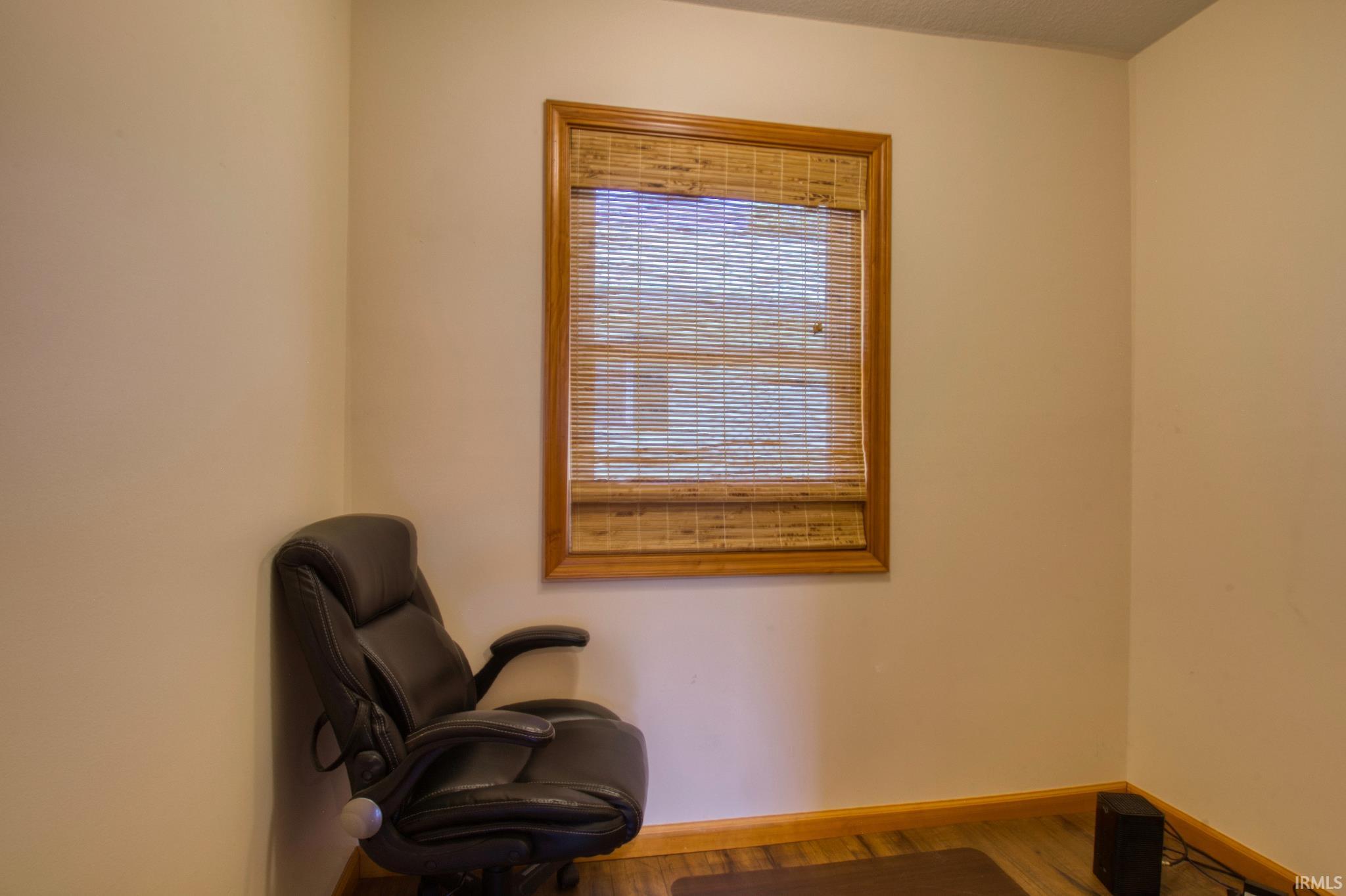 Room featuring a window with a wood-framed trim and a woven wood shade, light-toned wall paint, wood-finish flooring, and a baseboard molding