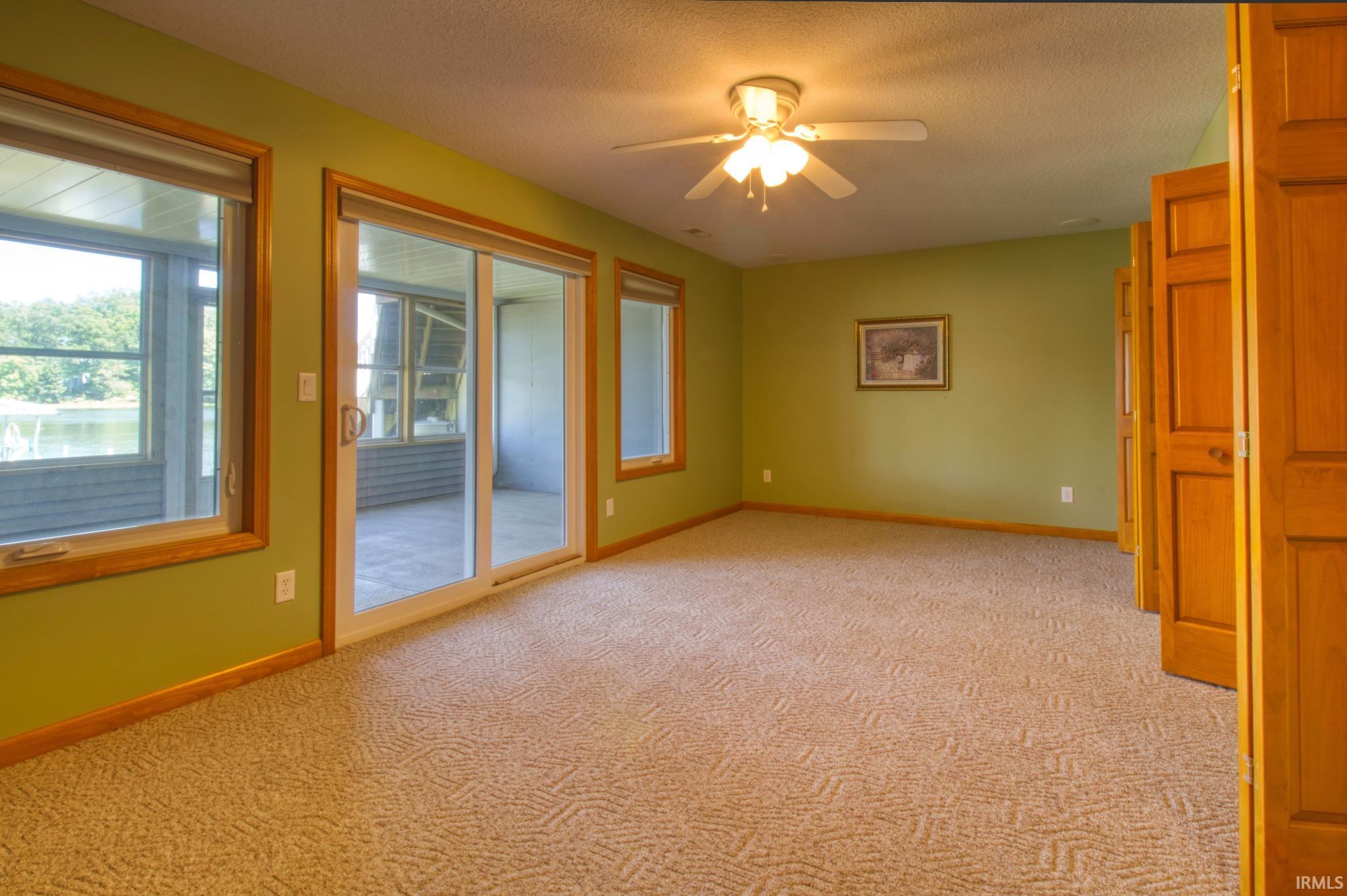 Carpeted interior space featuring wood-trim windows, a sliding glass door opening to an enclosed porch, and a ceiling fan with integrated lighting