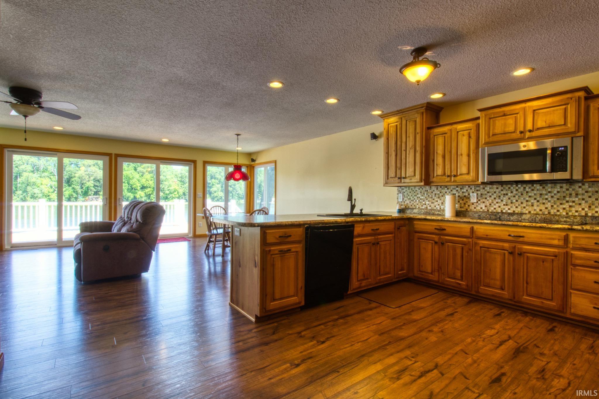 Open-concept kitchen and living area featuring wood-finish flooring, recessed lighting, and a ceiling fan
