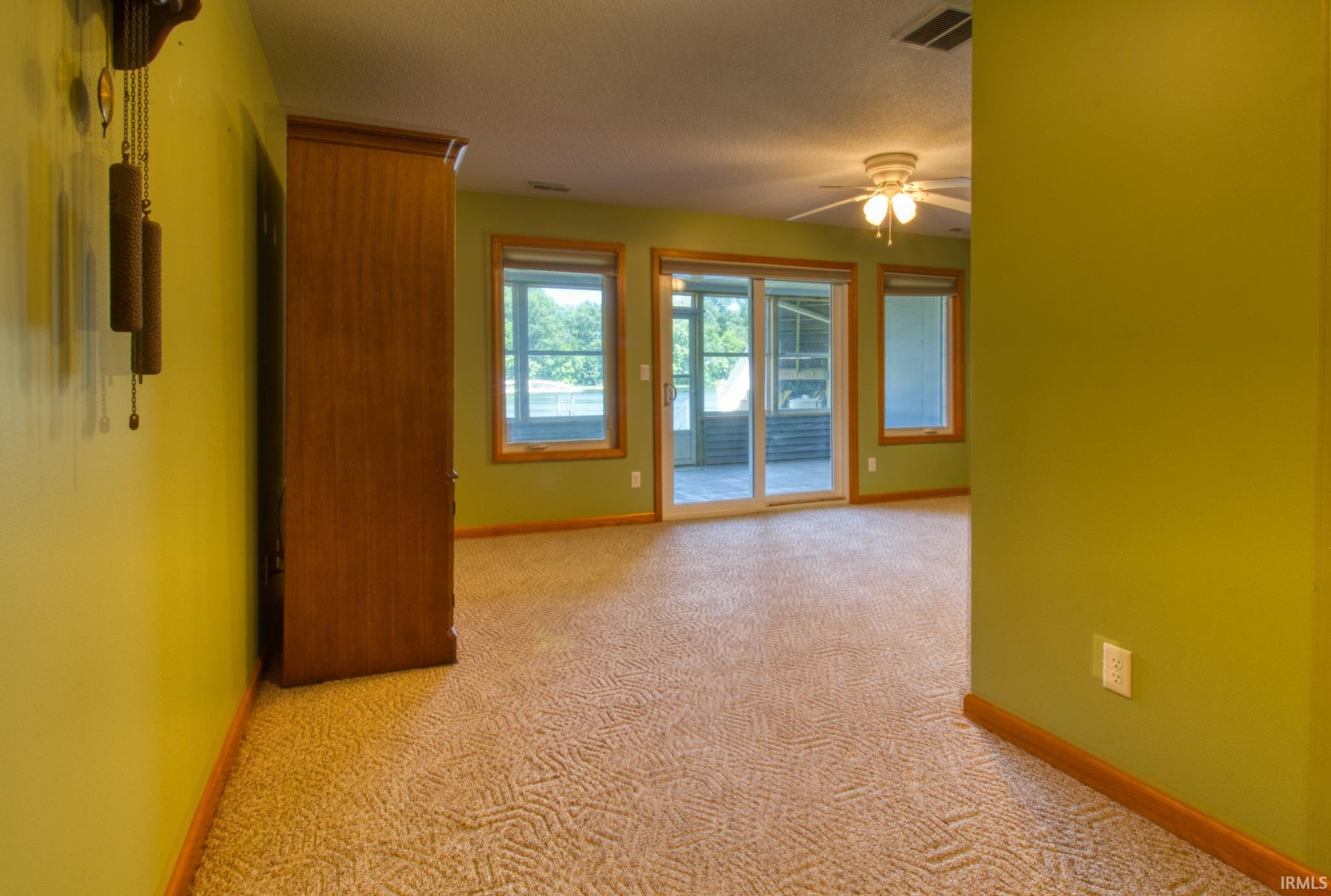 Carpeted interior space featuring a ceiling fan with light fixture, multiple windows, and a sliding glass door opening to an outdoor screened area
