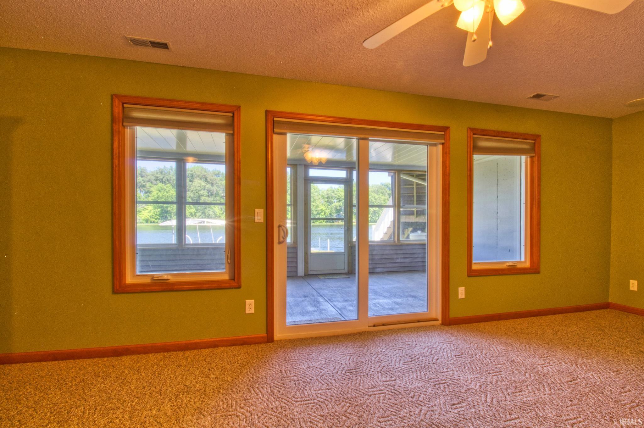 Room with patterned carpet flooring, a ceiling fan with integrated lighting, and three windows featuring wood trim
