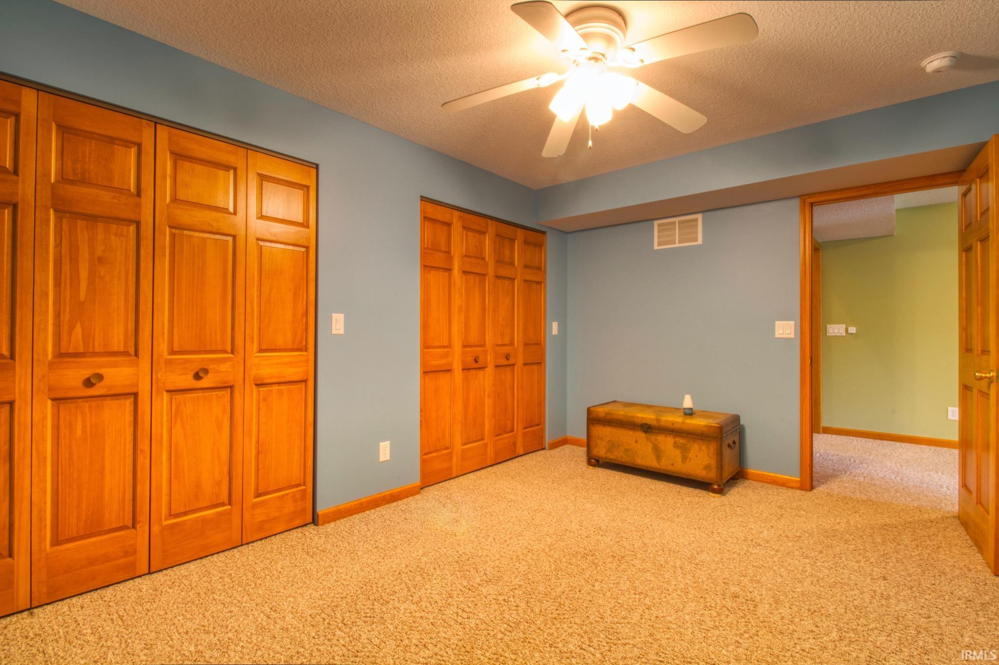 Carpeted Den  featuring two sets of bi-fold wood doors, a ceiling fan with integrated lighting, and light blue walls