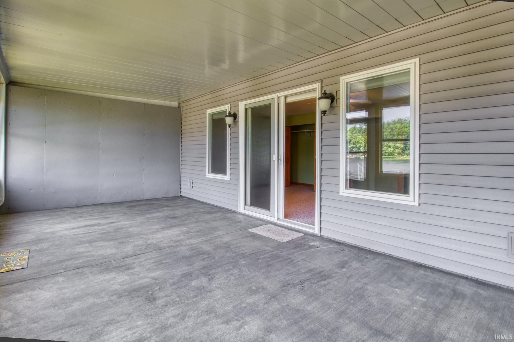 Covered concrete patio featuring a sliding glass door entry, two exterior wall sconces, and vinyl siding