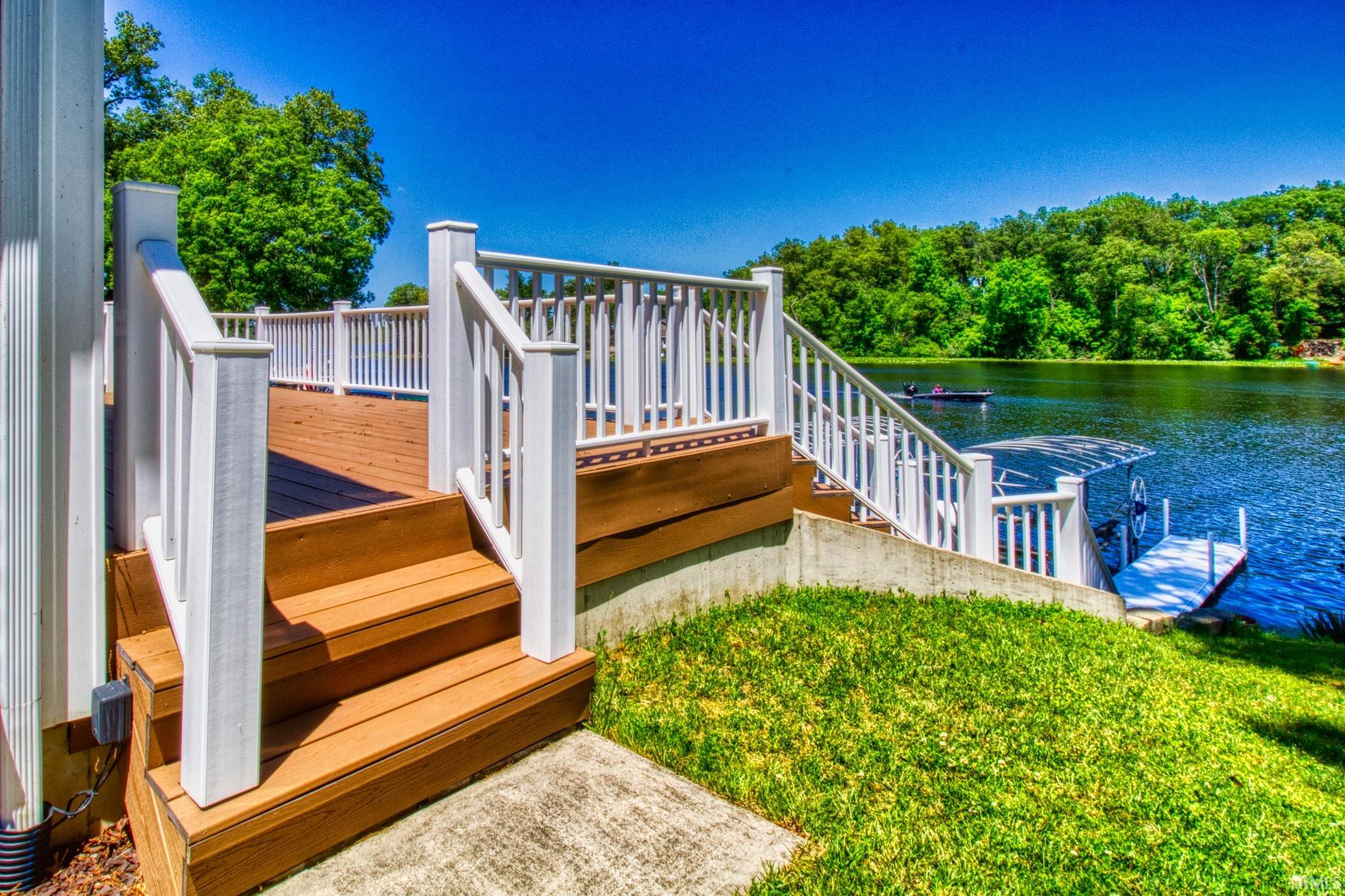 Multi-level deck with white railings and wood-finish flooring, leading to a private dock with a boat lift