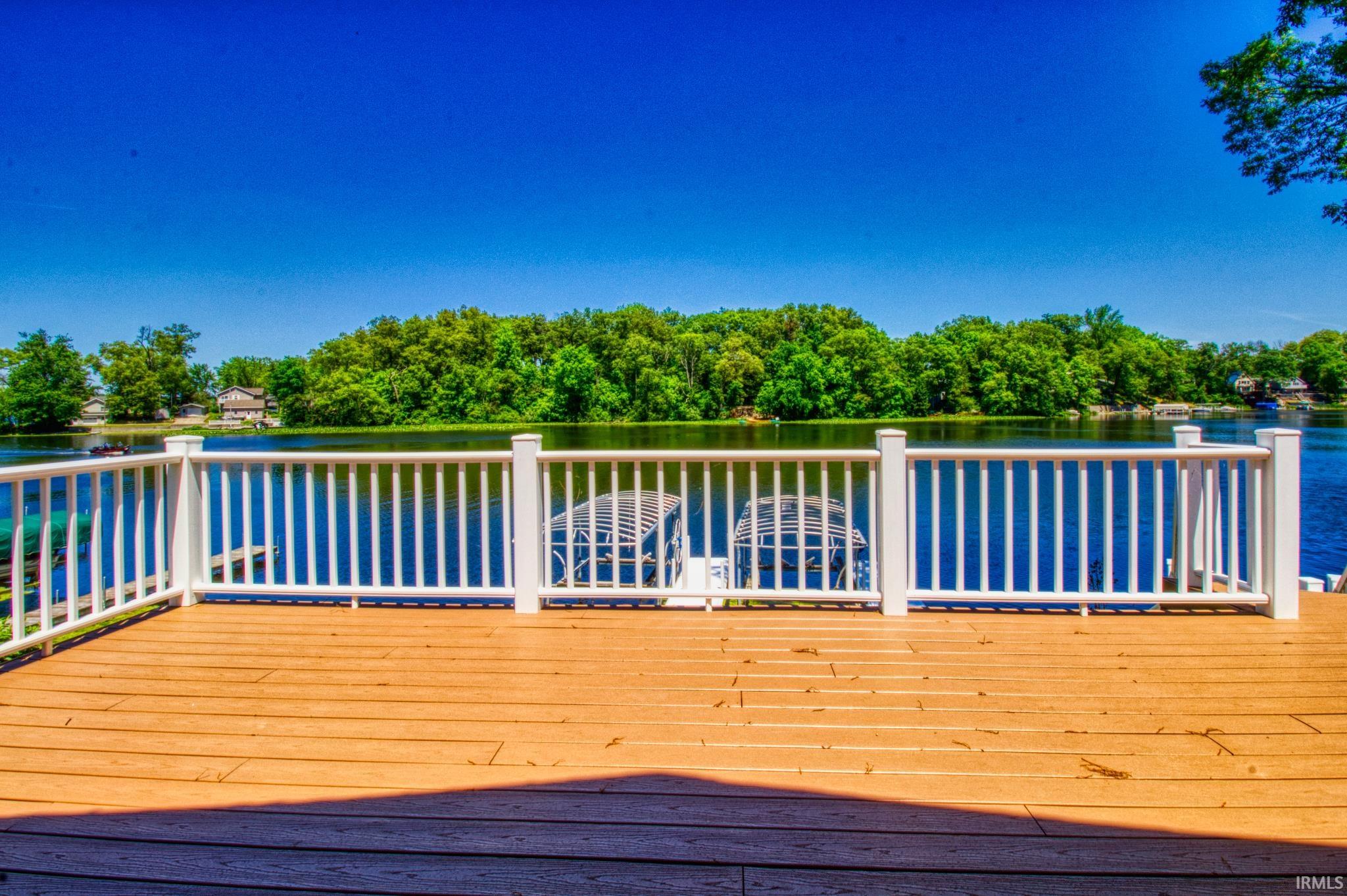 Expansive outdoor deck with composite decking and white railing, overlooking a serene body of water with lush green trees lining the distant shore