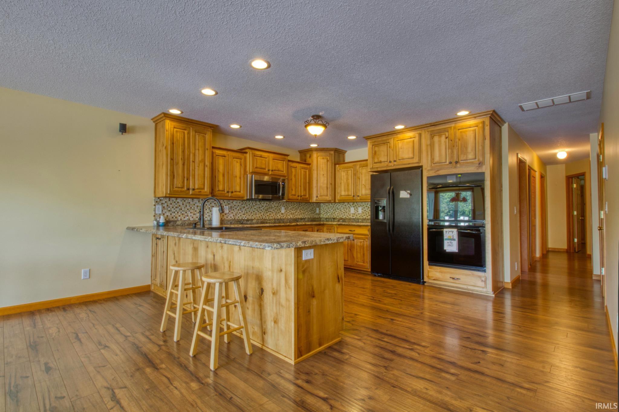 Spacious kitchen featuring wood-finish flooring, custom cabinetry, granite countertops, and a tile mosaic backsplash