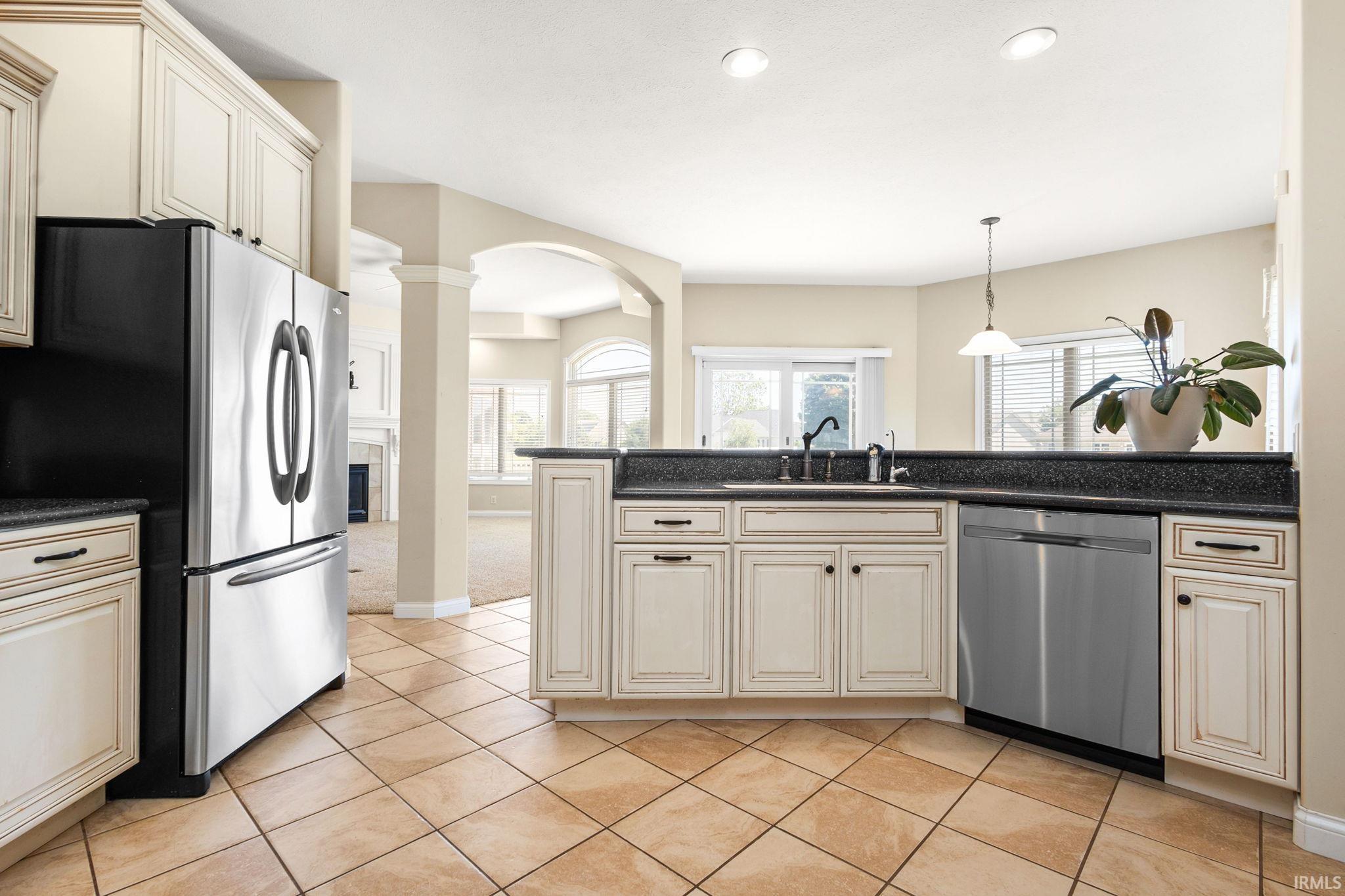 Kitchen featuring diagonal tile flooring, cream-colored cabinetry with dark hardware, a stainless steel refrigerator, and a dark countertop with an undermount sink and faucet