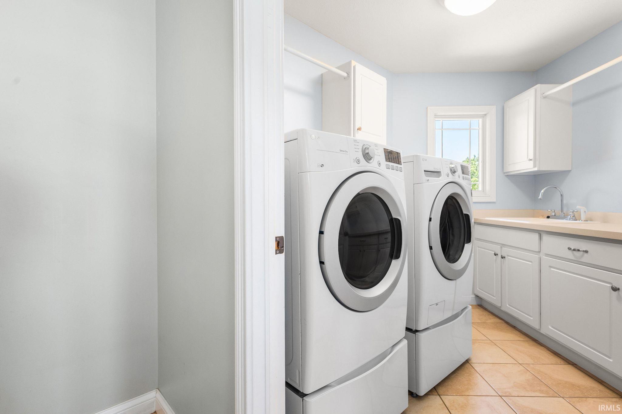 Dedicated laundry room featuring front-loading appliances, white cabinetry, and a utility sink