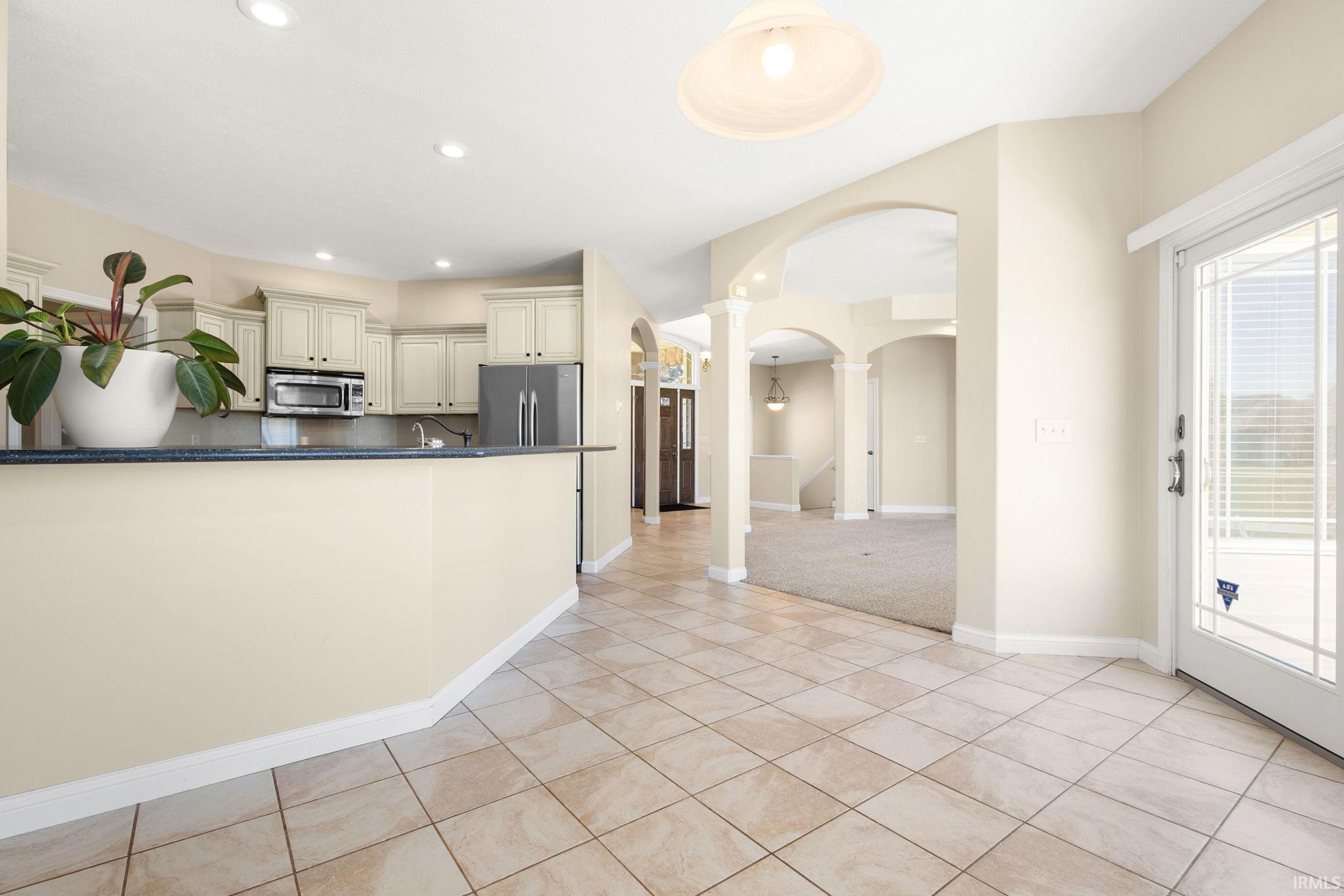 Tiled entryway with a glass-paned door, opening into a space with a breakfast bar, kitchen cabinetry, and integrated appliances