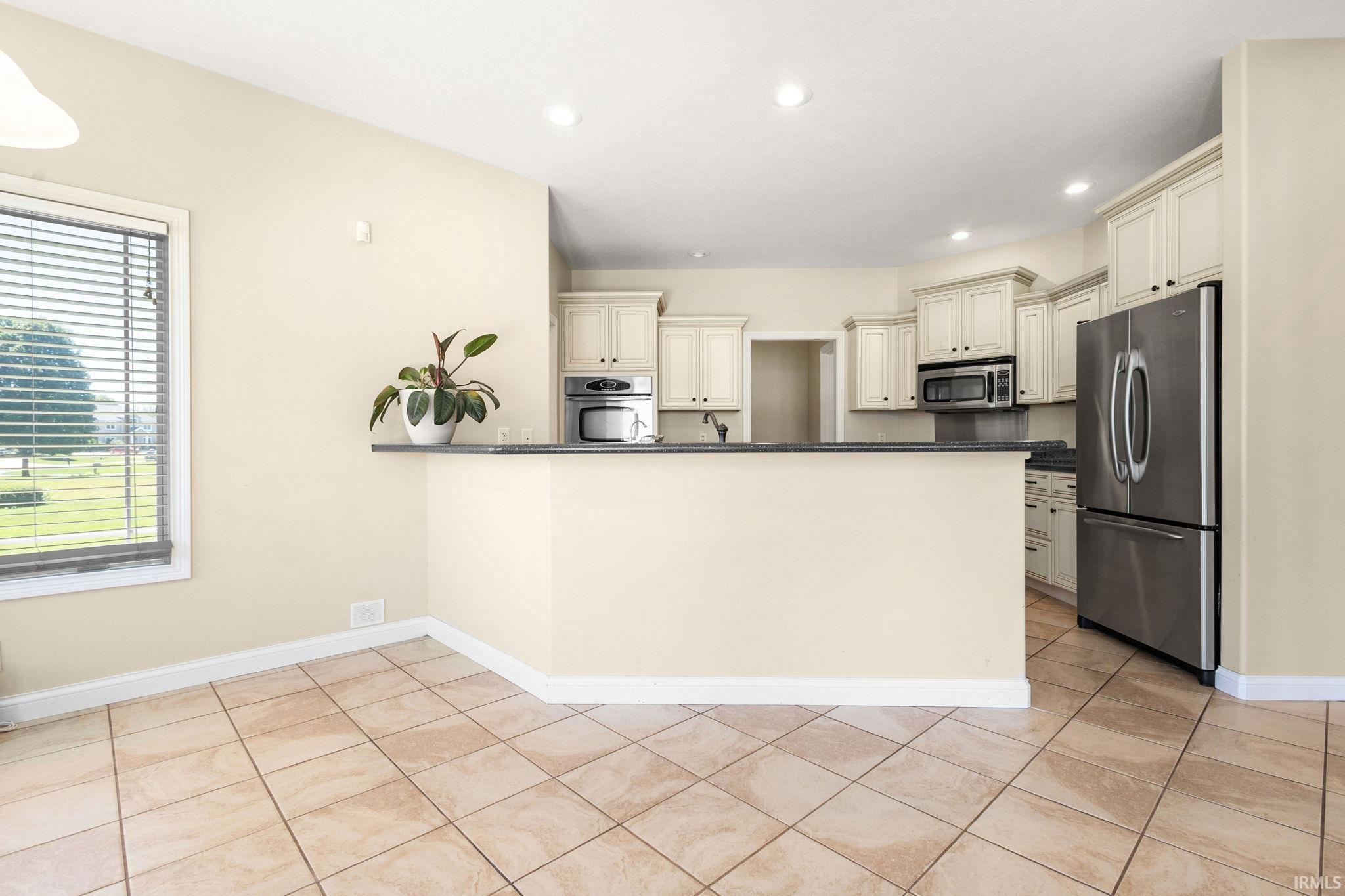 Kitchen area featuring cream cabinetry, stainless steel appliances, a breakfast bar with a dark countertop, and recessed lighting