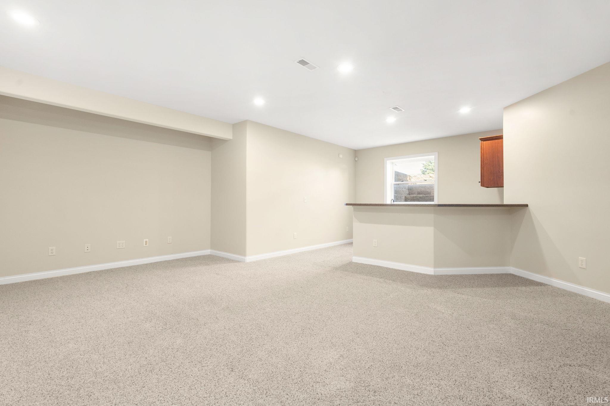 Spacious recreation room featuring neutral carpeting, recessed lighting, and a built-in wet bar area with wood-finish cabinetry