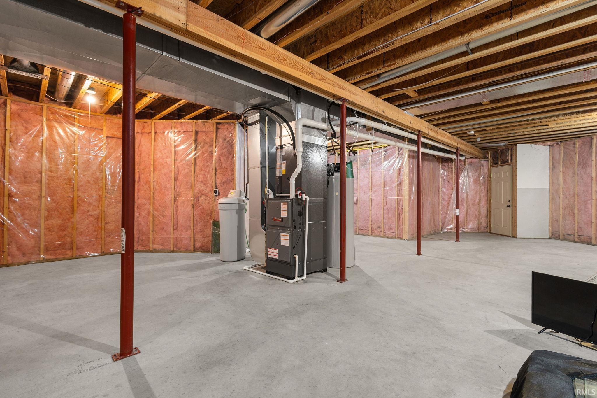 Spacious unfinished basement offering concrete flooring, exposed wood joists, framed perimeter walls with insulation, utility access, and stairwell access to garage