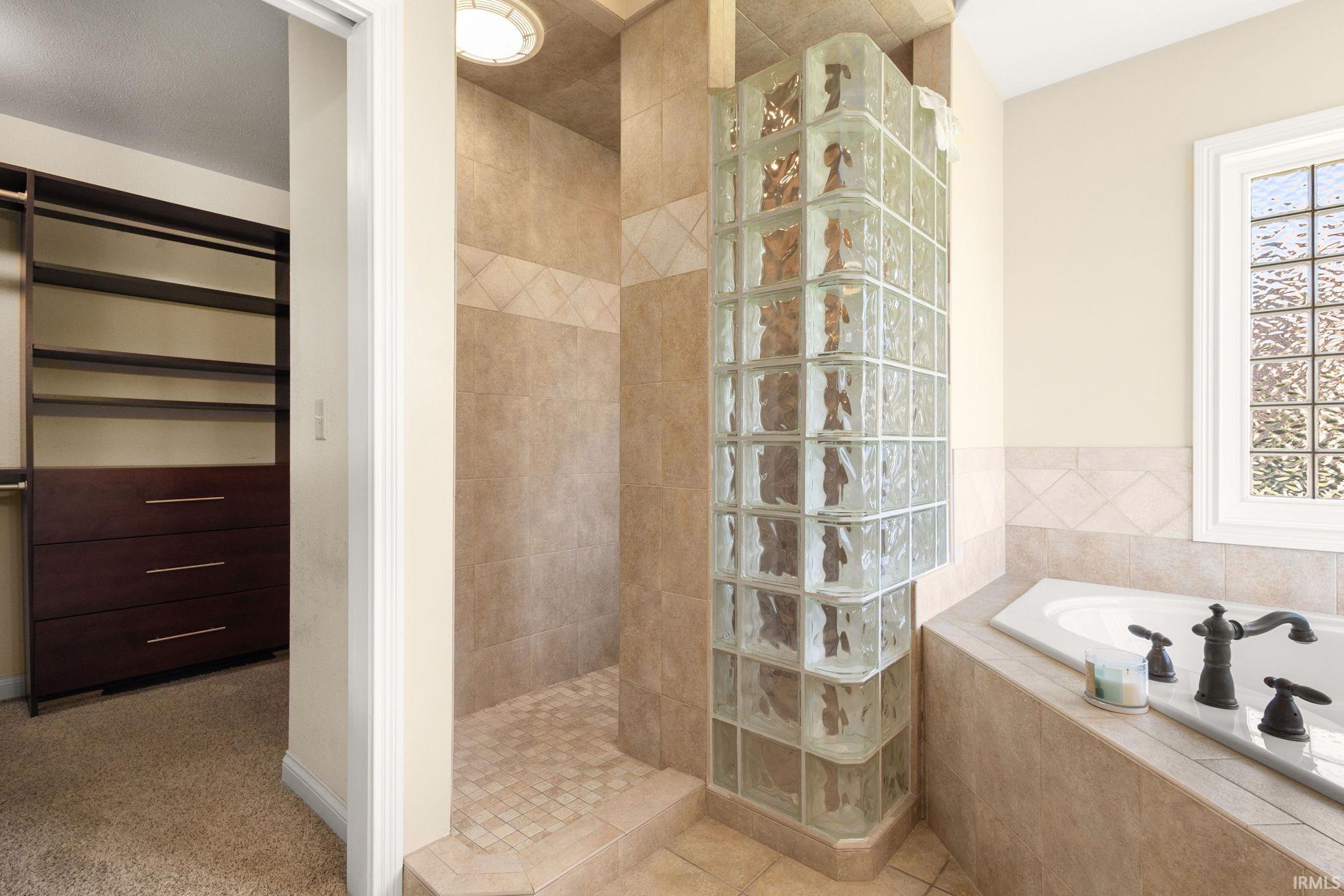 Tiled walk-in shower with a glass block enclosure, accompanied by a built-in soaking tub with dark bronze fixtures