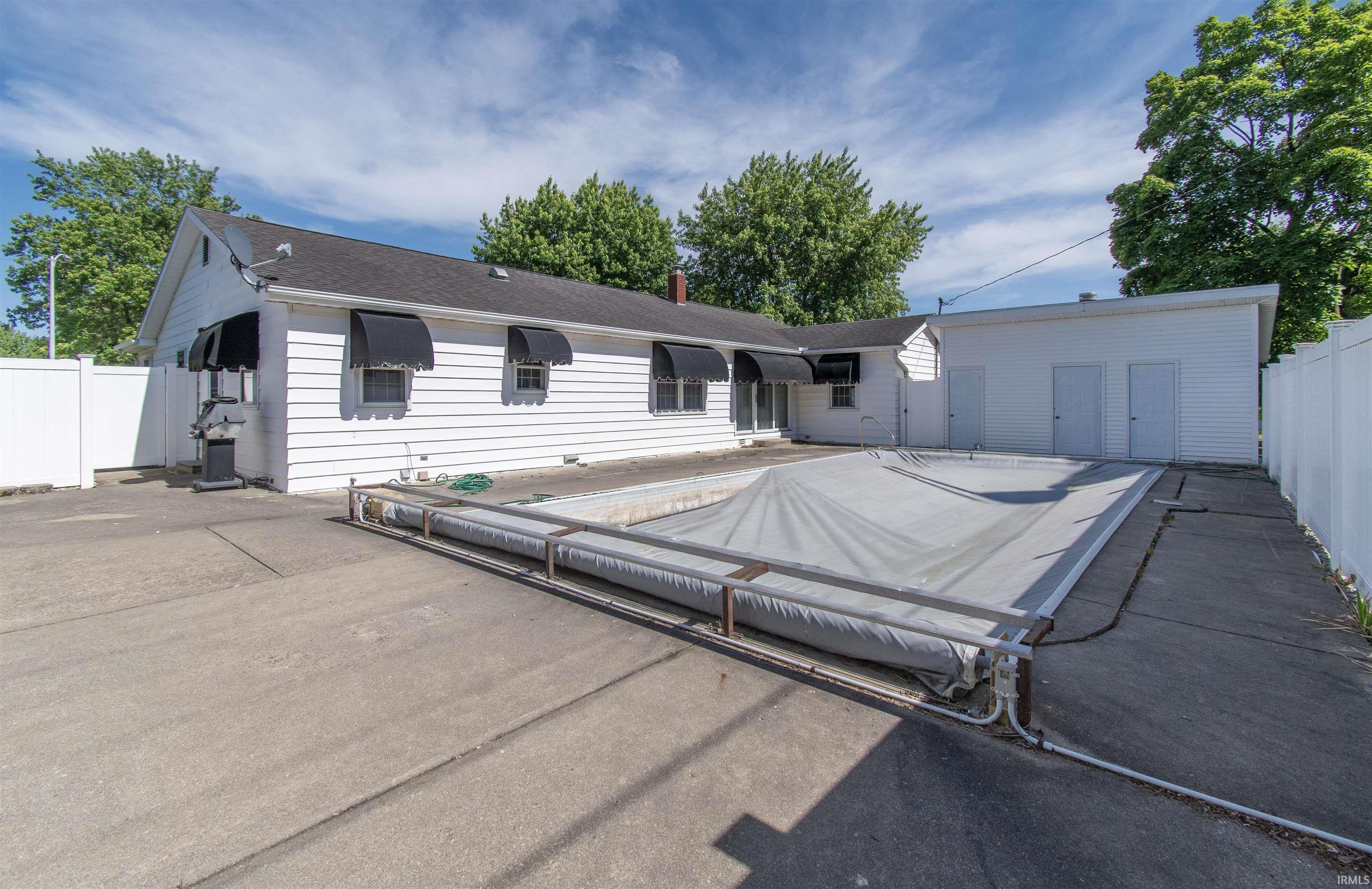 Exterior concrete patio featuring an in-ground pool with a protective cover, flanked by a white vinyl privacy fence