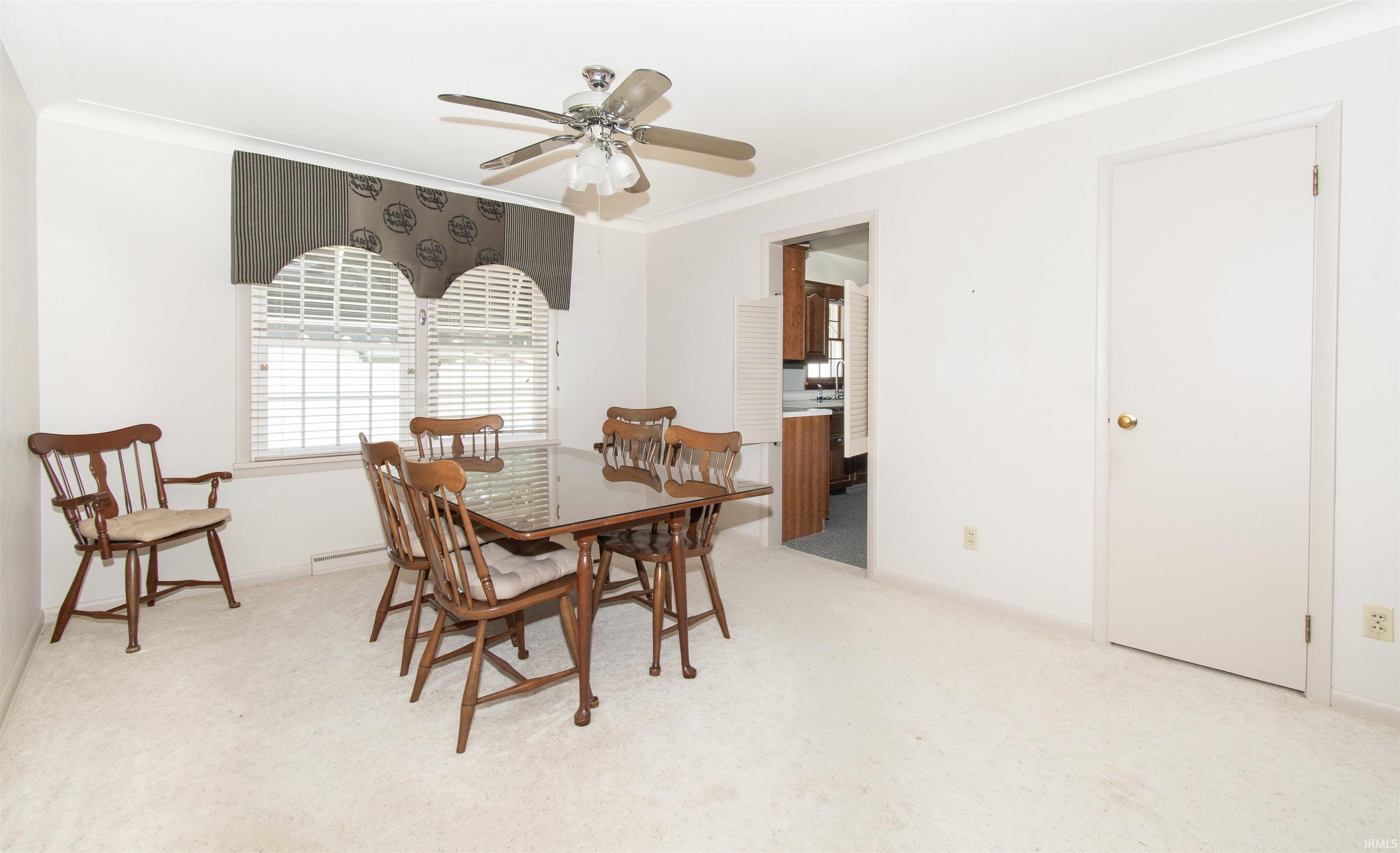 Carpeted room featuring a ceiling fan with integrated lighting, a window with horizontal blinds and a decorative valance, white trim, and a white interior door with a brass-tone doorknob