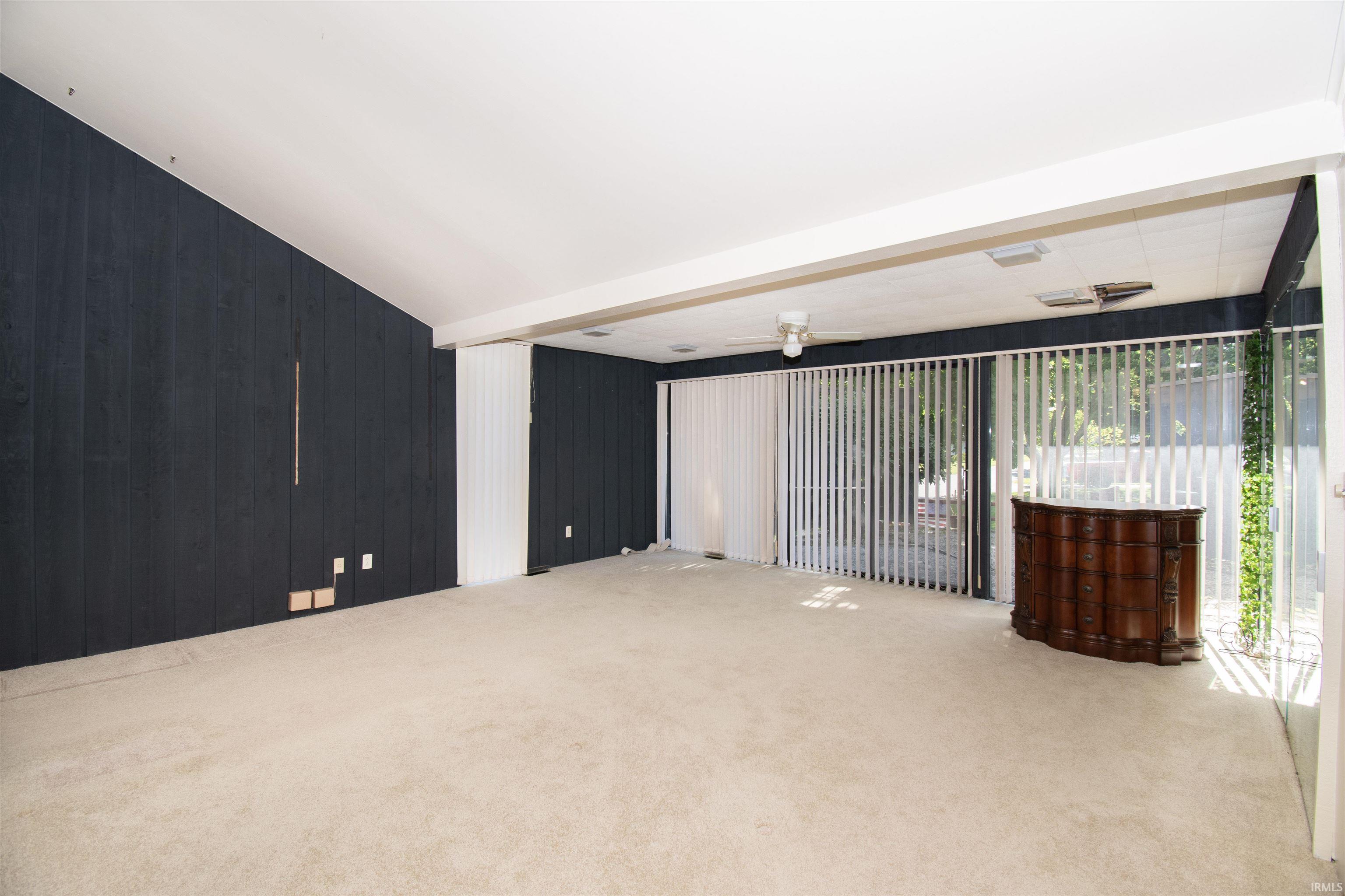 Spacious interior featuring a vaulted white ceiling, dark paneled accent wall, and light-colored carpeting