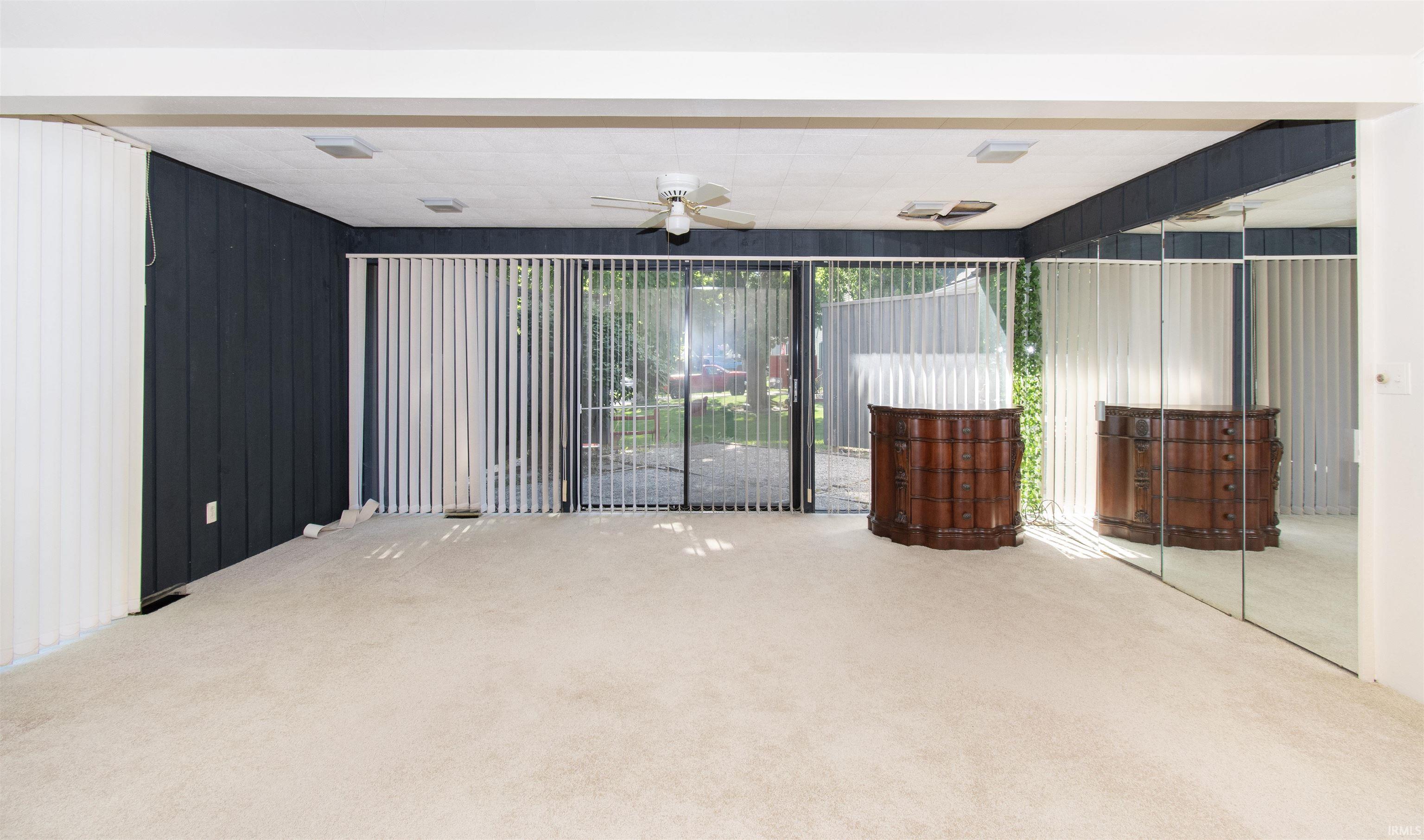 Spacious room featuring light-colored carpeting, dark-paneled walls, and a ceiling fan