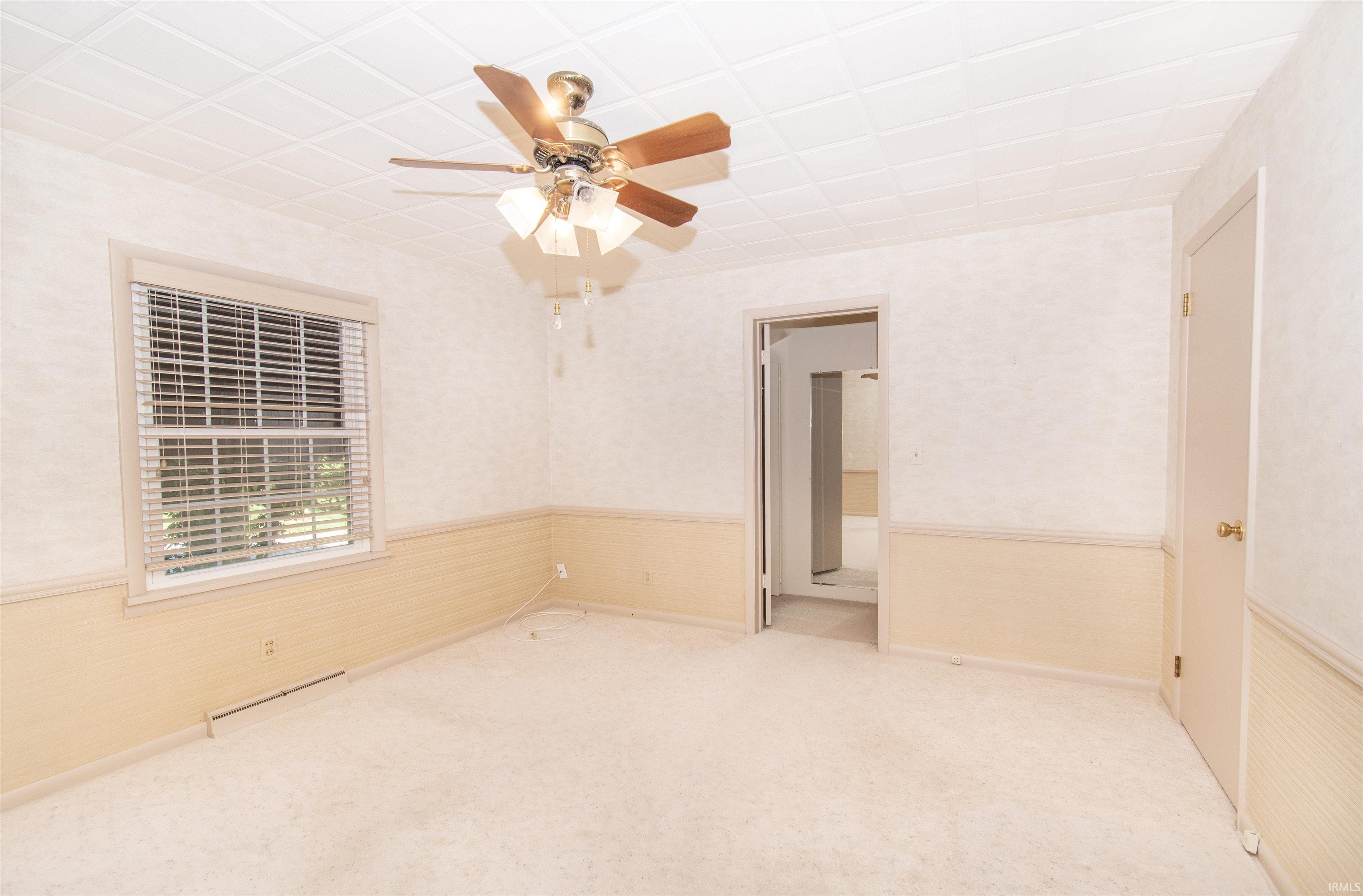 Soft-toned bedroom with neutral carpeting, a ceiling fan with integrated lighting, and a white paneled ceiling