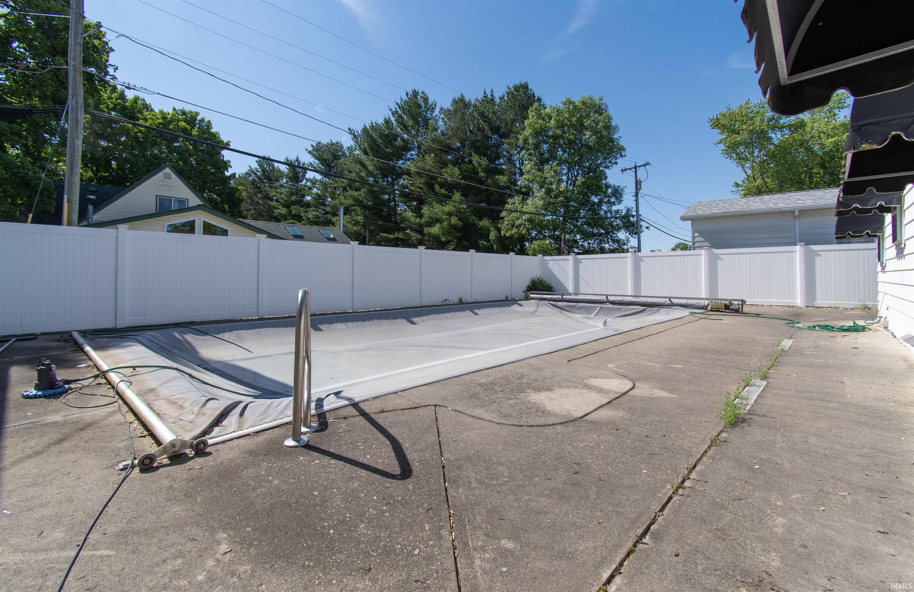 Concrete patio featuring an in-ground pool with a cover and a perimeter white vinyl fence