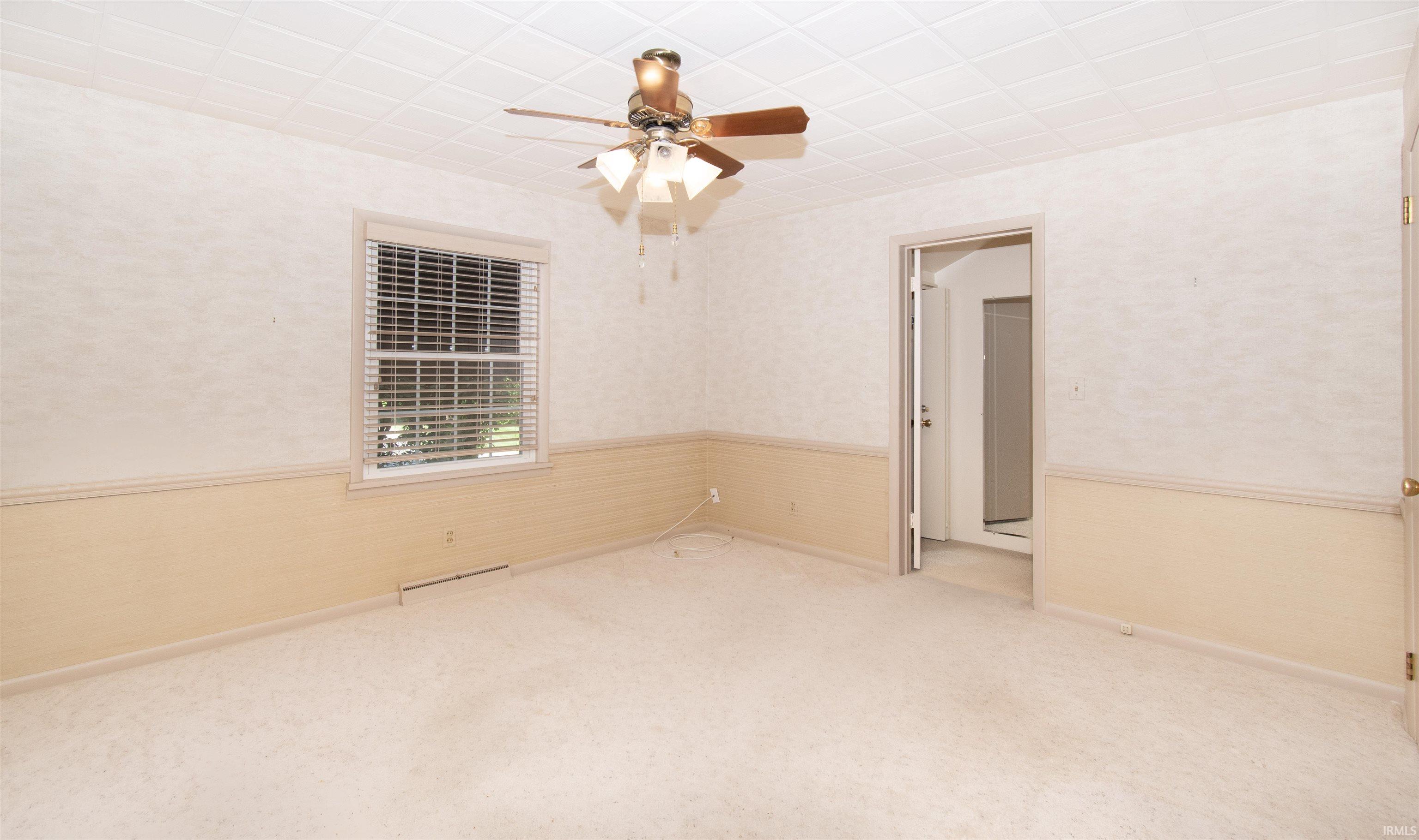 Spacious room featuring carpeted flooring, a ceiling fan with light fixture, and a window with blinds