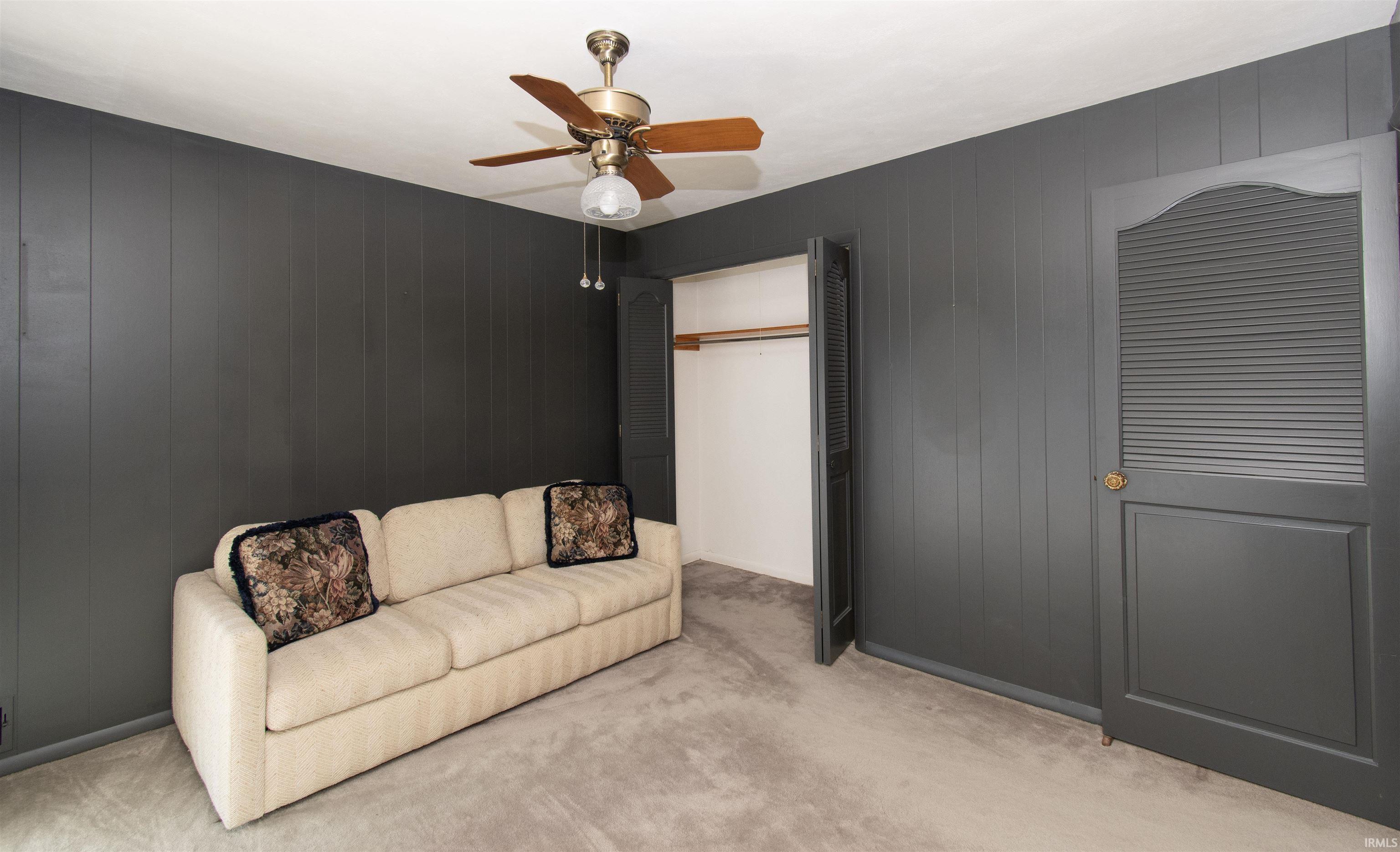 Room featuring vertical wall paneling, a ceiling fan with integrated lighting, and neutral tone carpeting