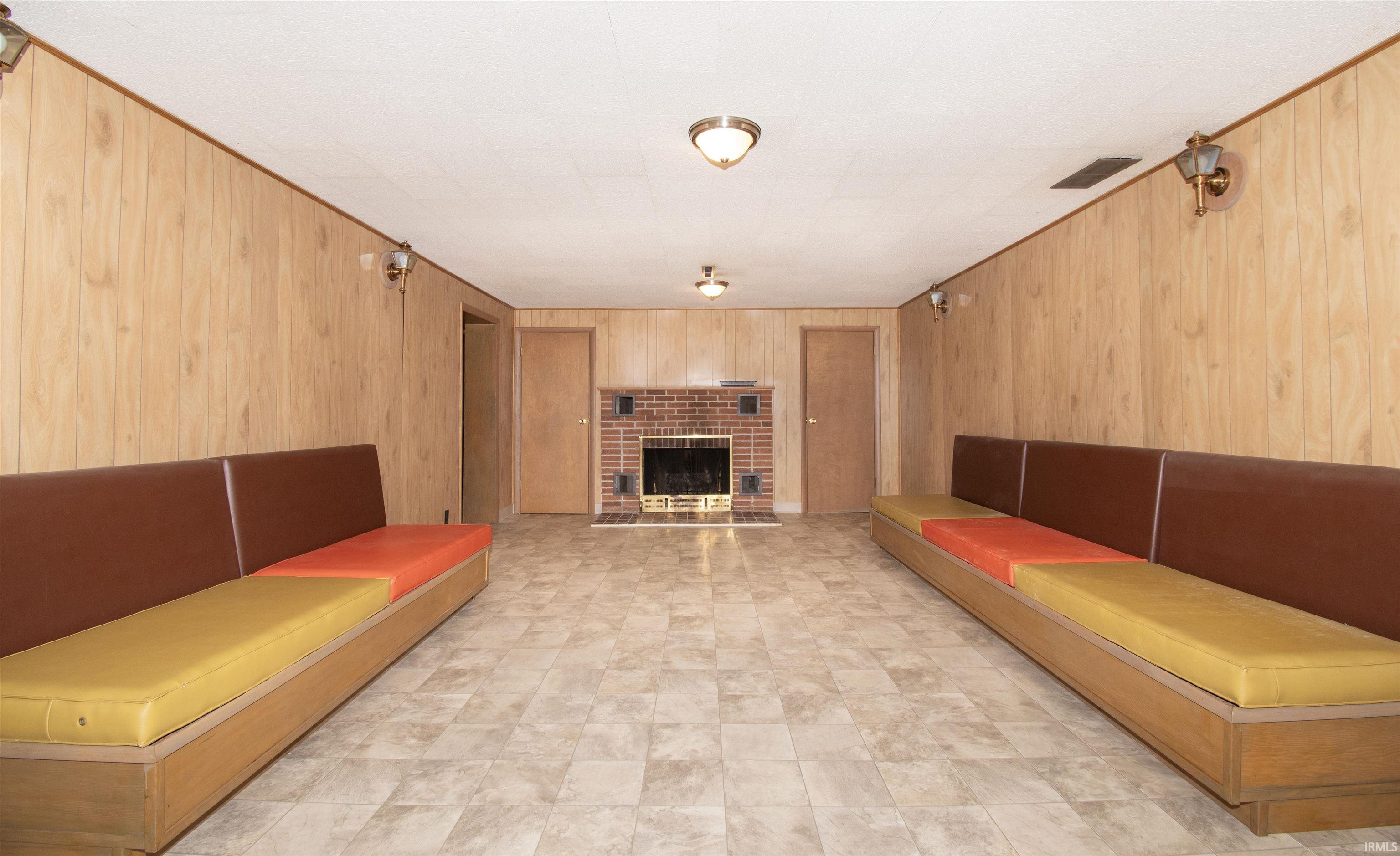 Spacious room featuring wood paneling, a brick fireplace, and durable tile flooring