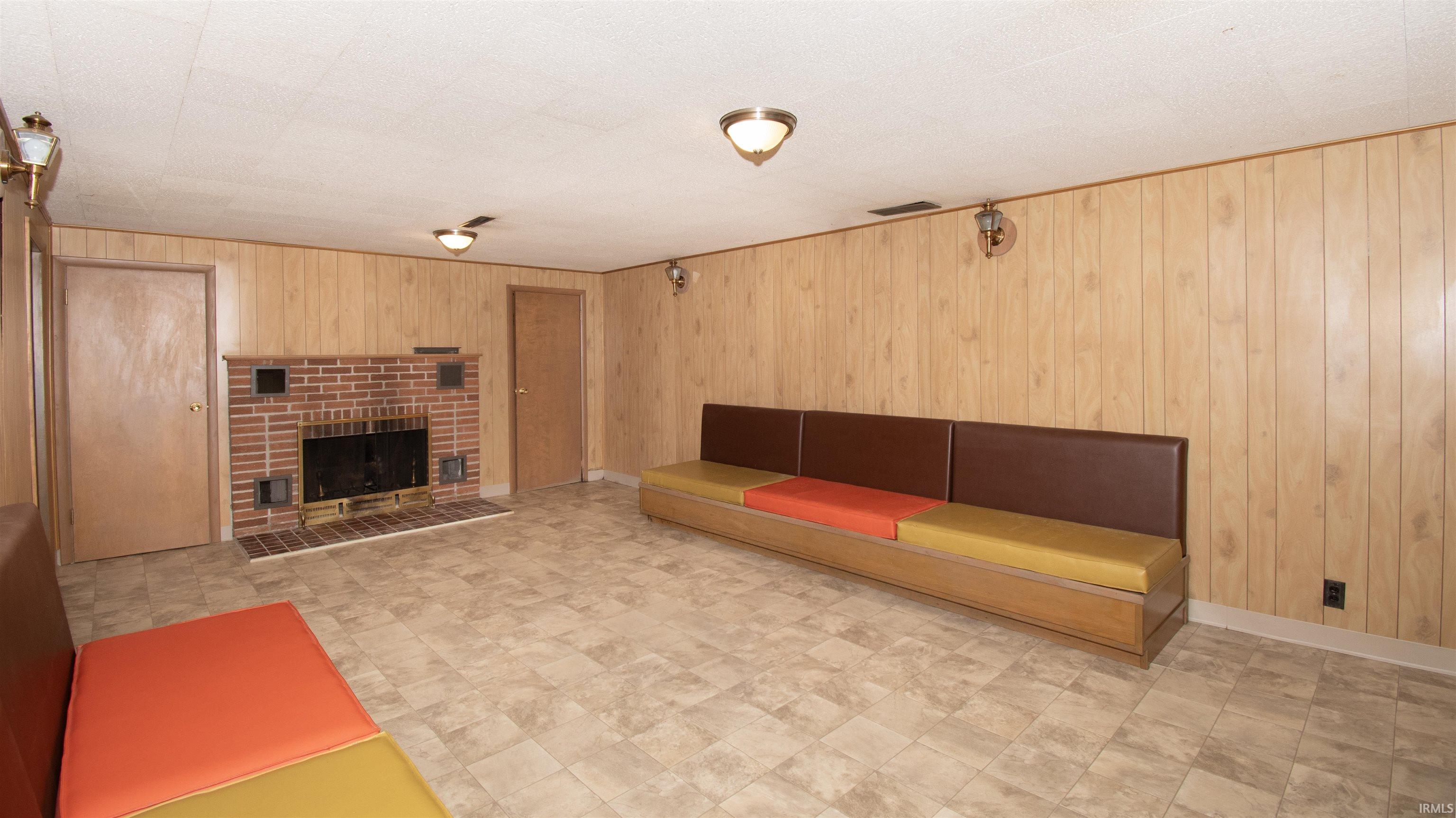 Spacious room featuring wood-panel walls, patterned floor tiles, and a prominent brick fireplace with a metal grate
