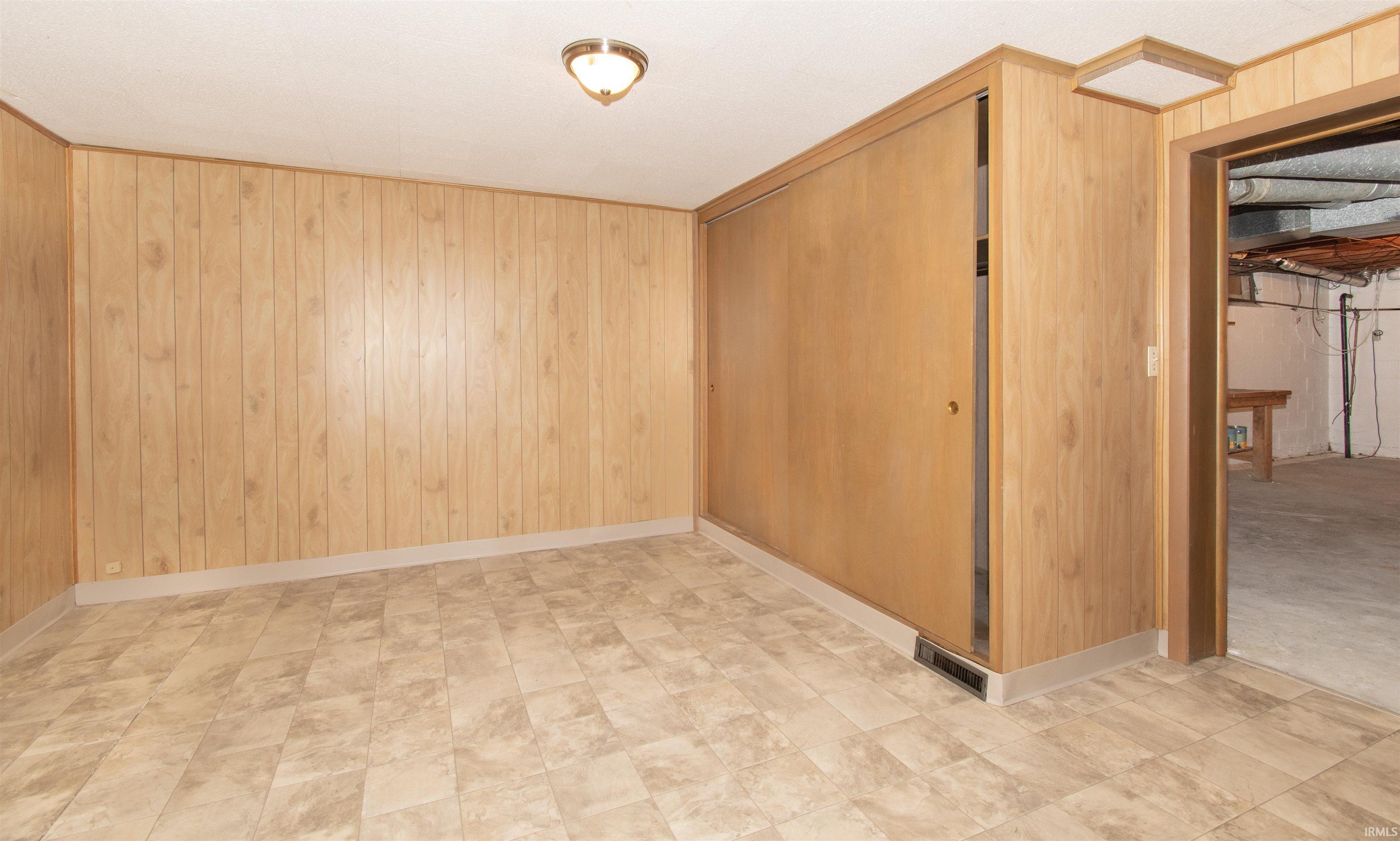Room featuring light wood-panel walls, patterned tile flooring, and a flush-mount ceiling light