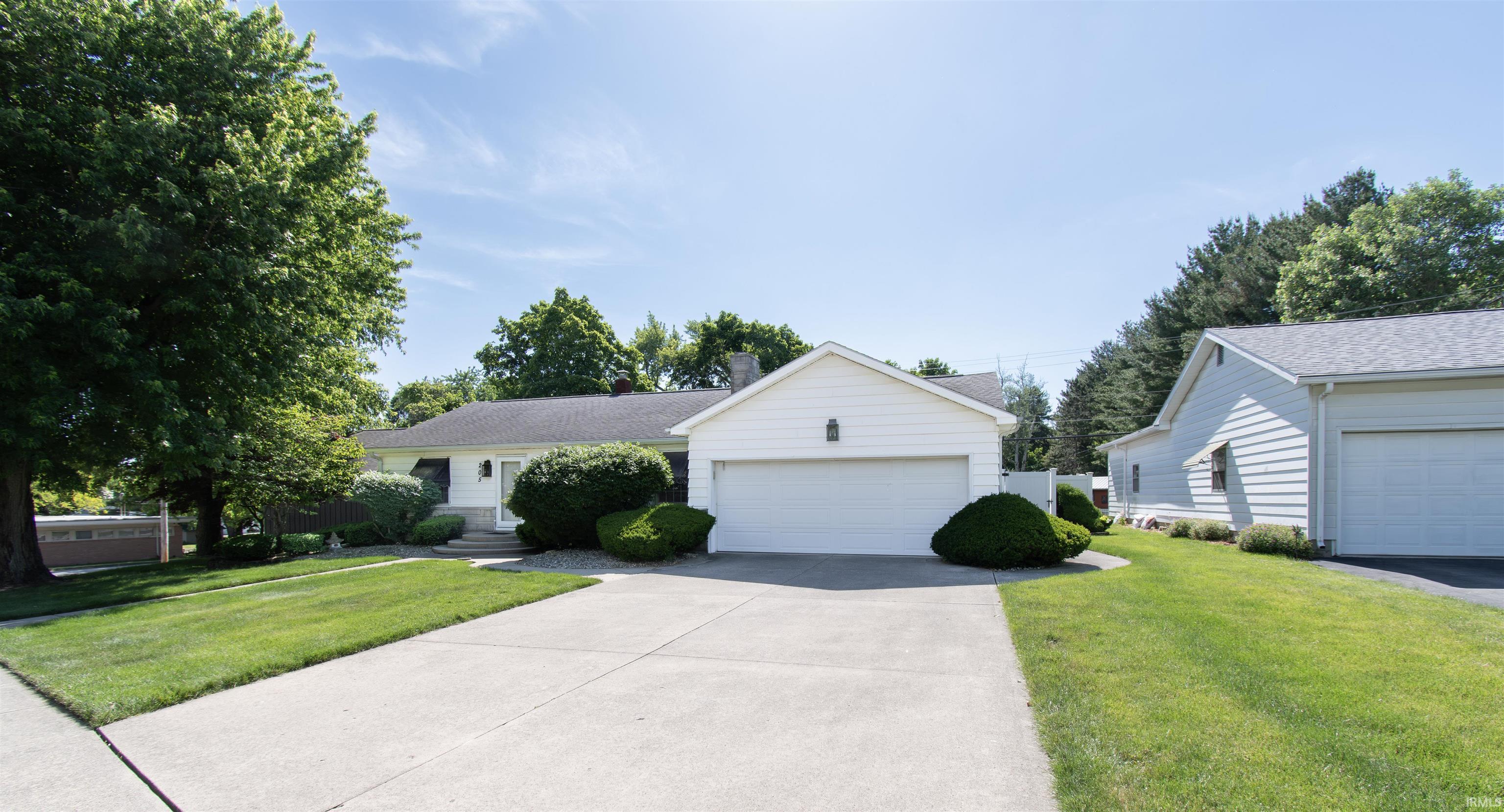 White exterior architecture featuring an attached two-car garage and a detached garage, a concrete driveway, and mature landscaping