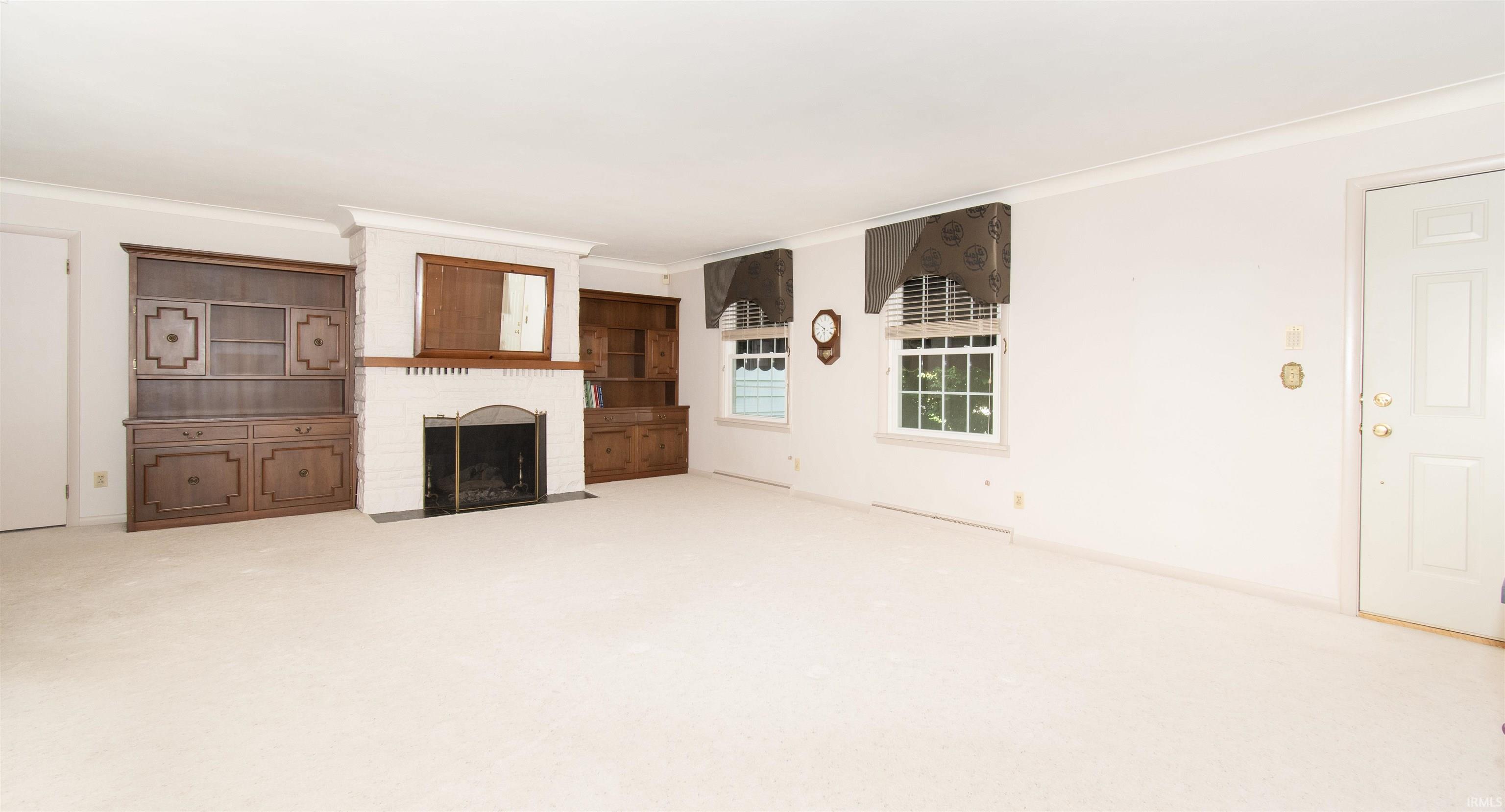 Bright living area featuring a white brick fireplace with a wood mantle, built-in wood cabinetry, and neutral carpeting