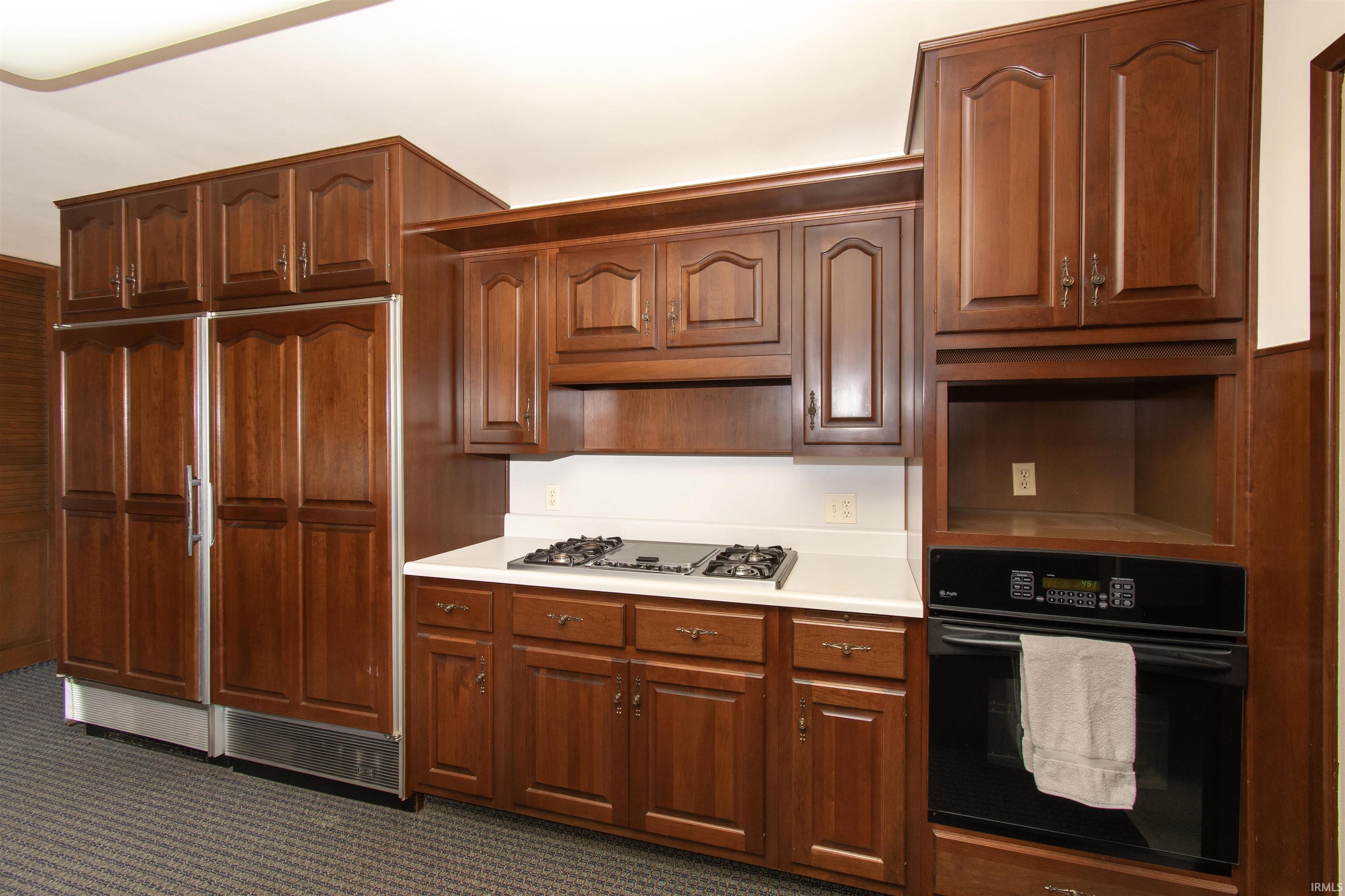 Kitchen featuring custom wood cabinetry, integrated panel-front refrigerator and freezer, built-in oven, gas cooktop, and white countertops