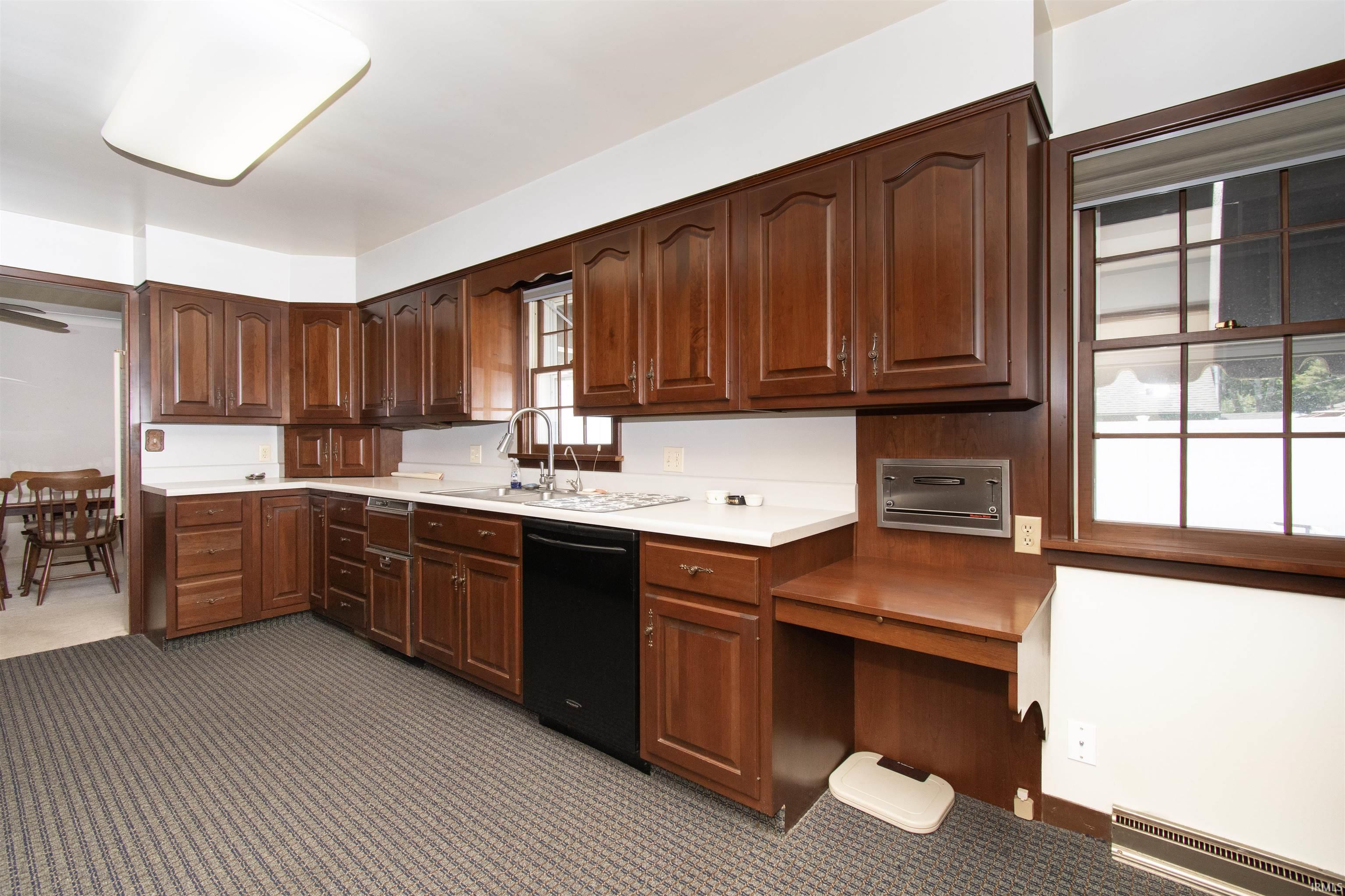 Spacious kitchen featuring extensive wood-finish cabinetry, white countertops, and a black built-in dishwasher