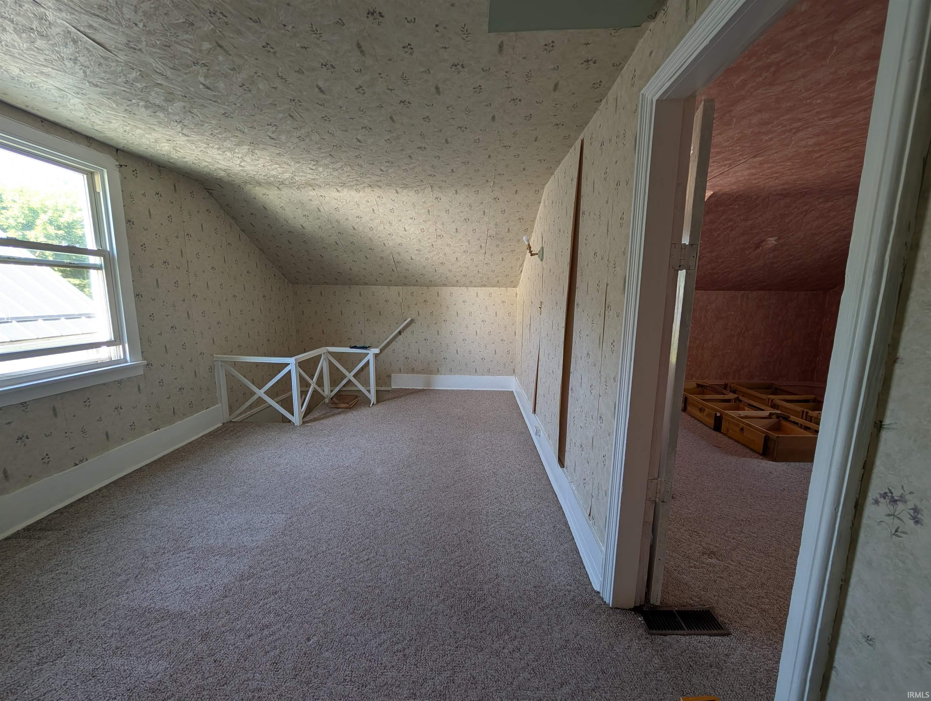 Carpeted attic space featuring a window, sloped ceilings, and wallpapered walls