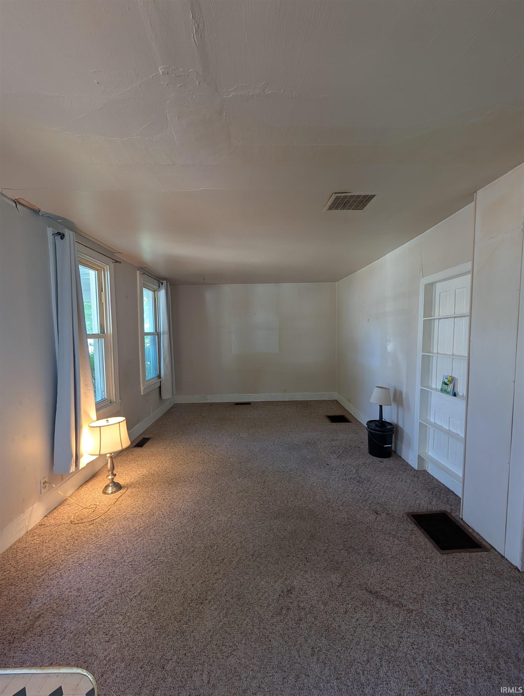 Carpeted interior space featuring white walls and multiple windows