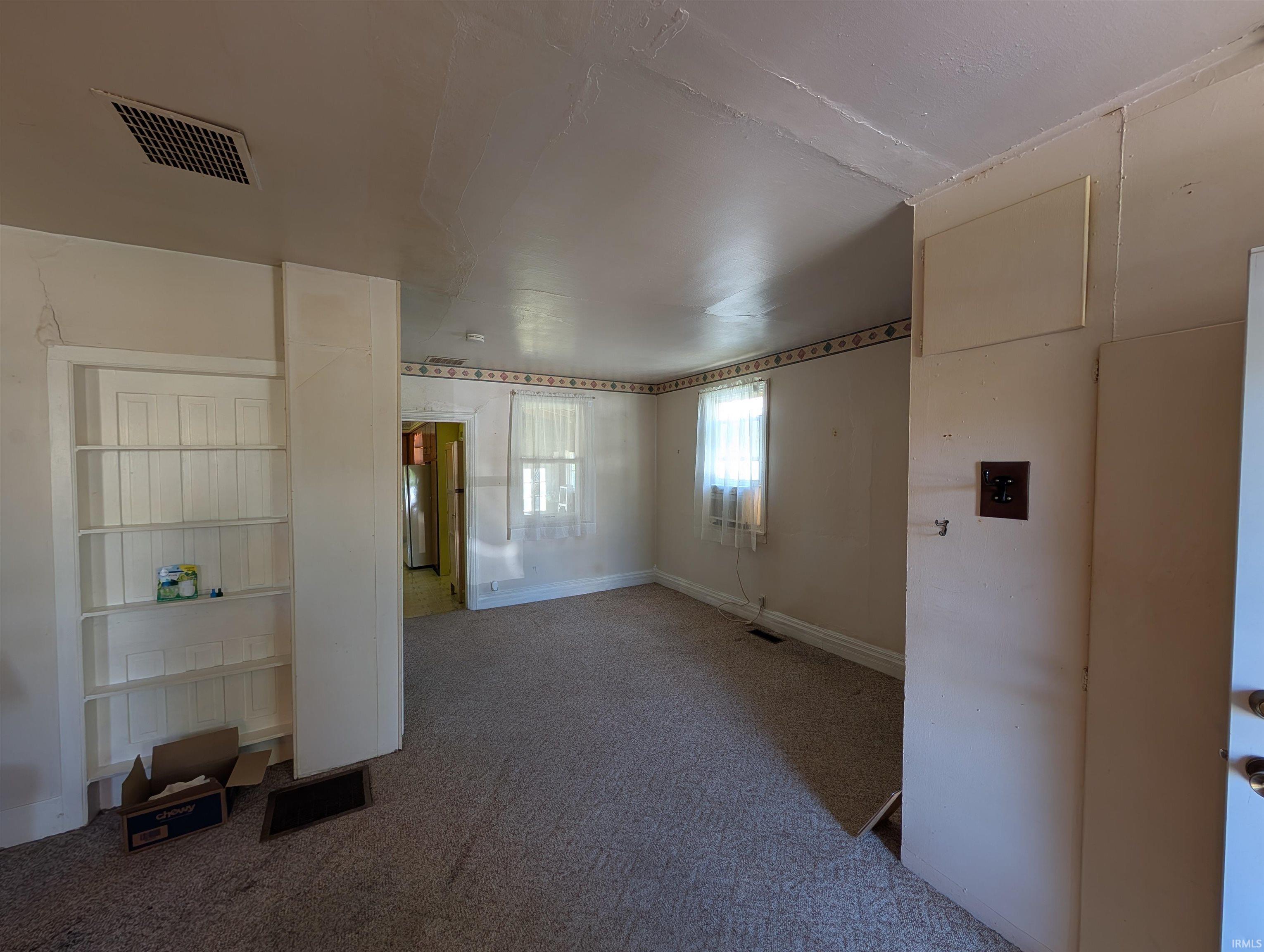 Room featuring carpet flooring, built-in shelving, two windows, and a ceiling vent