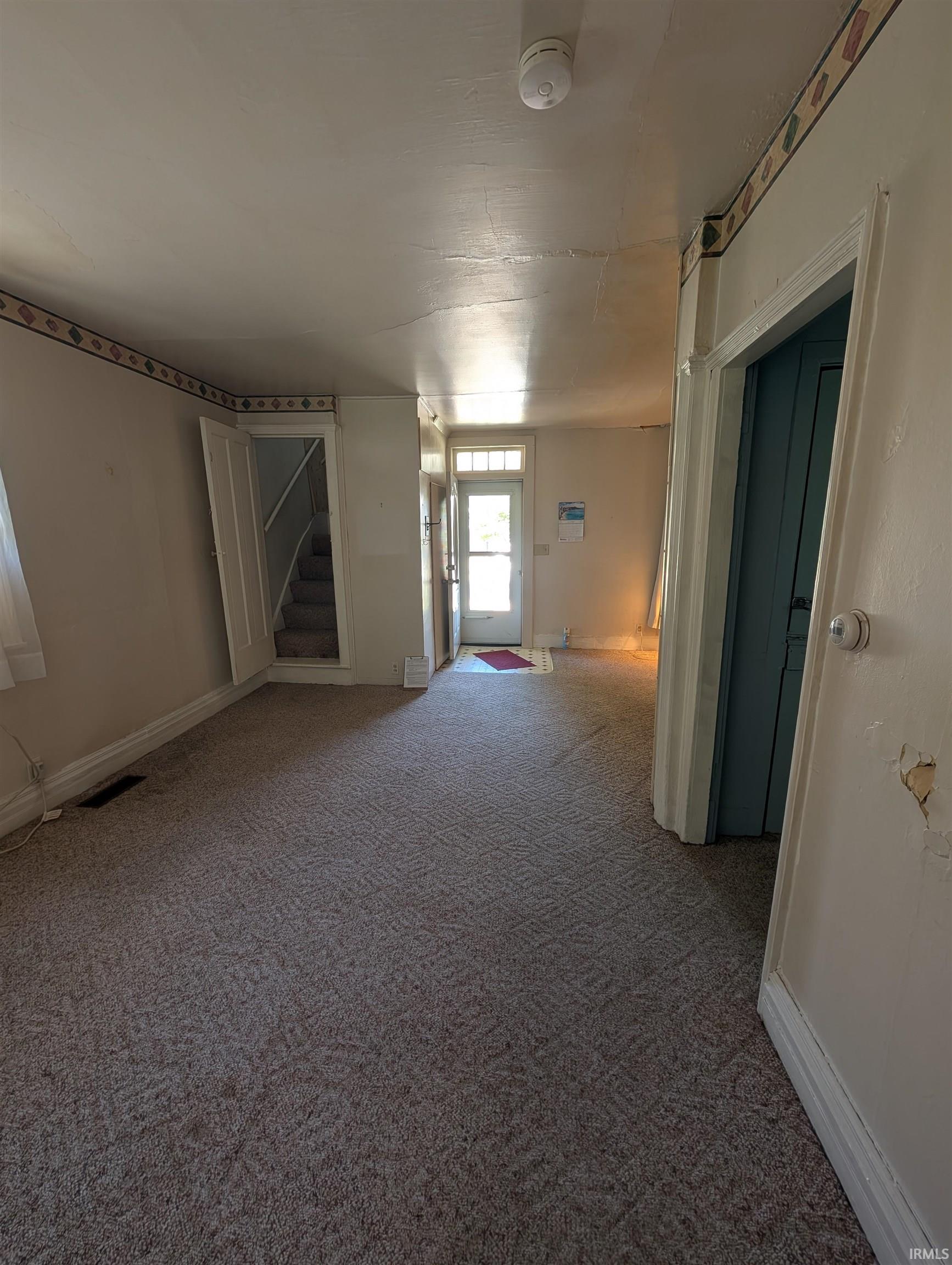Spacious room featuring patterned carpeting, light-toned walls with decorative border, and a visible doorway leading to a staircase