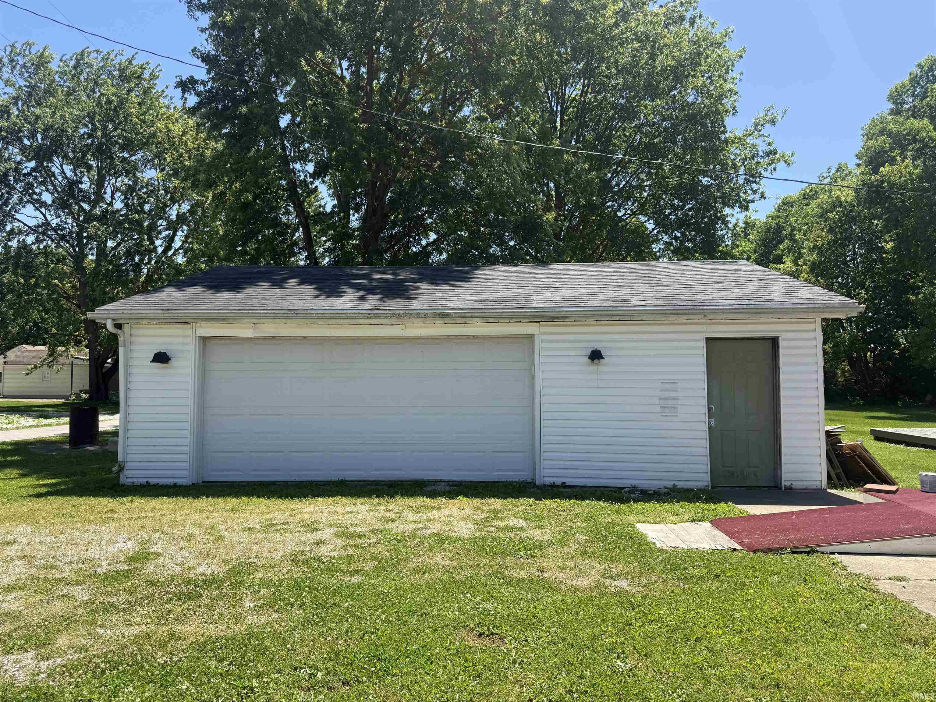 Detached garage featuring white vinyl siding, a two-car garage door, and a single entry door