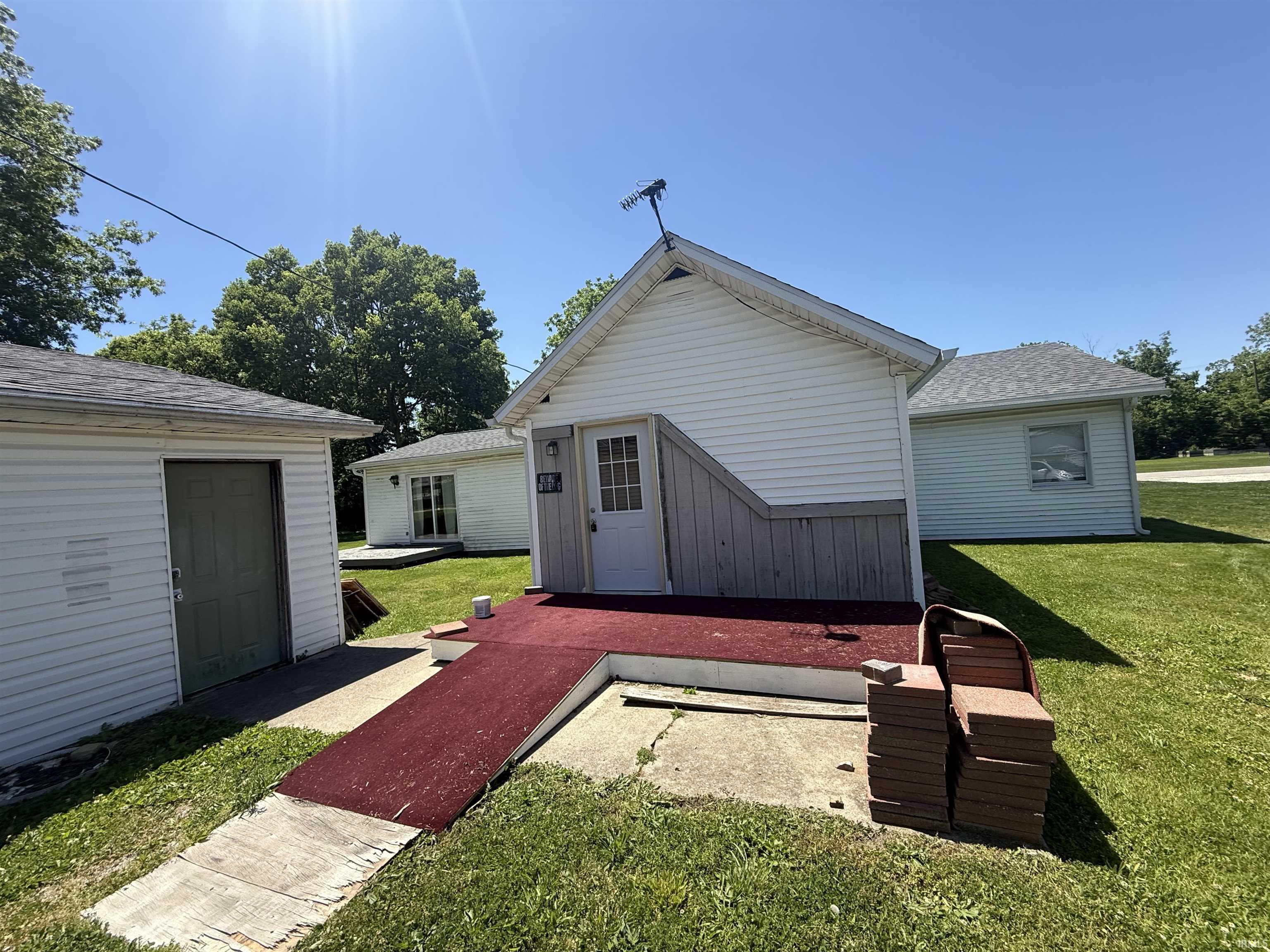 Exterior featuring white horizontal siding, a red carpeted ramp, and a detached single-door outbuilding