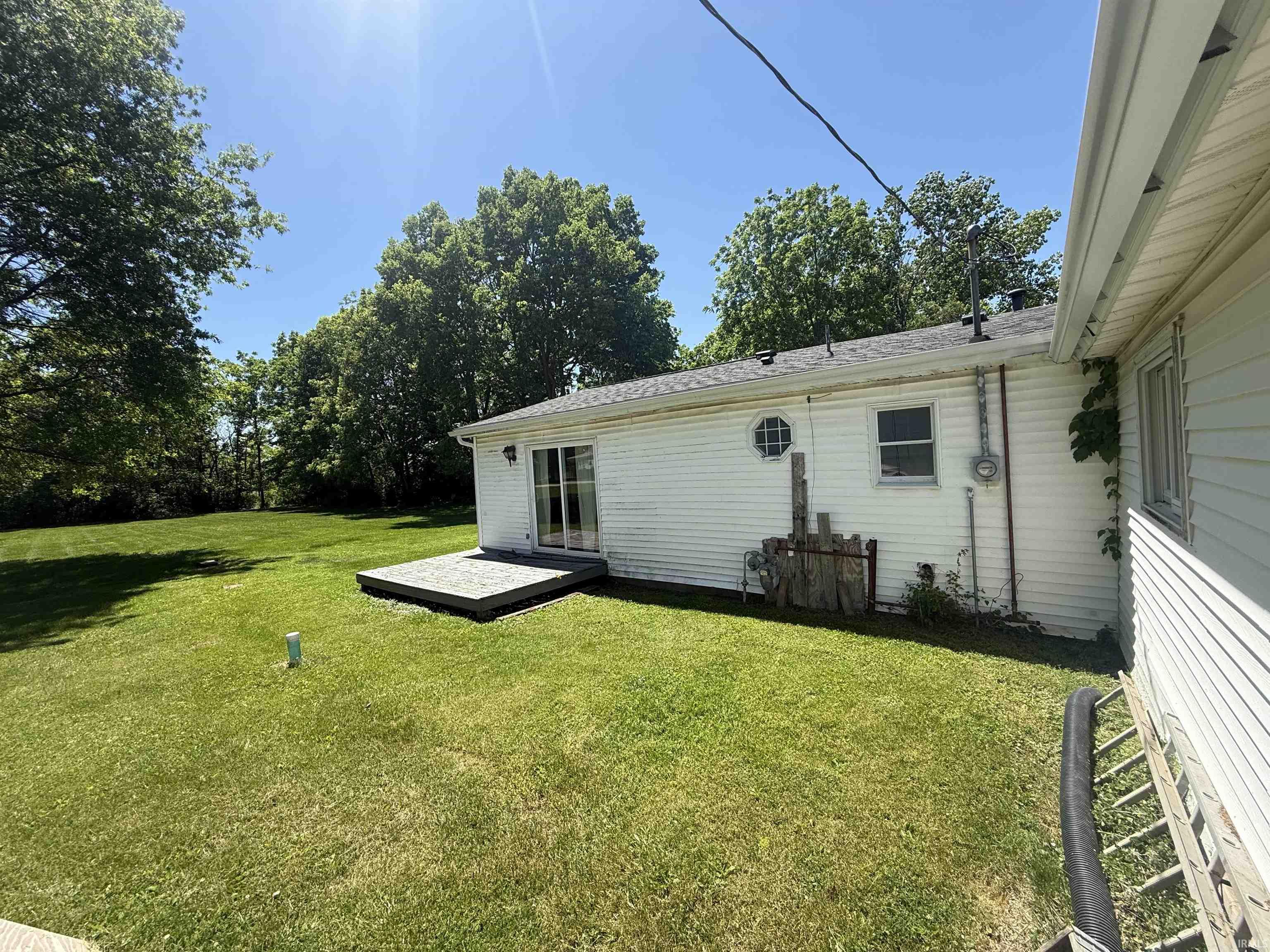 Rear exterior featuring white siding, a dark roof, and mature trees surrounding the property