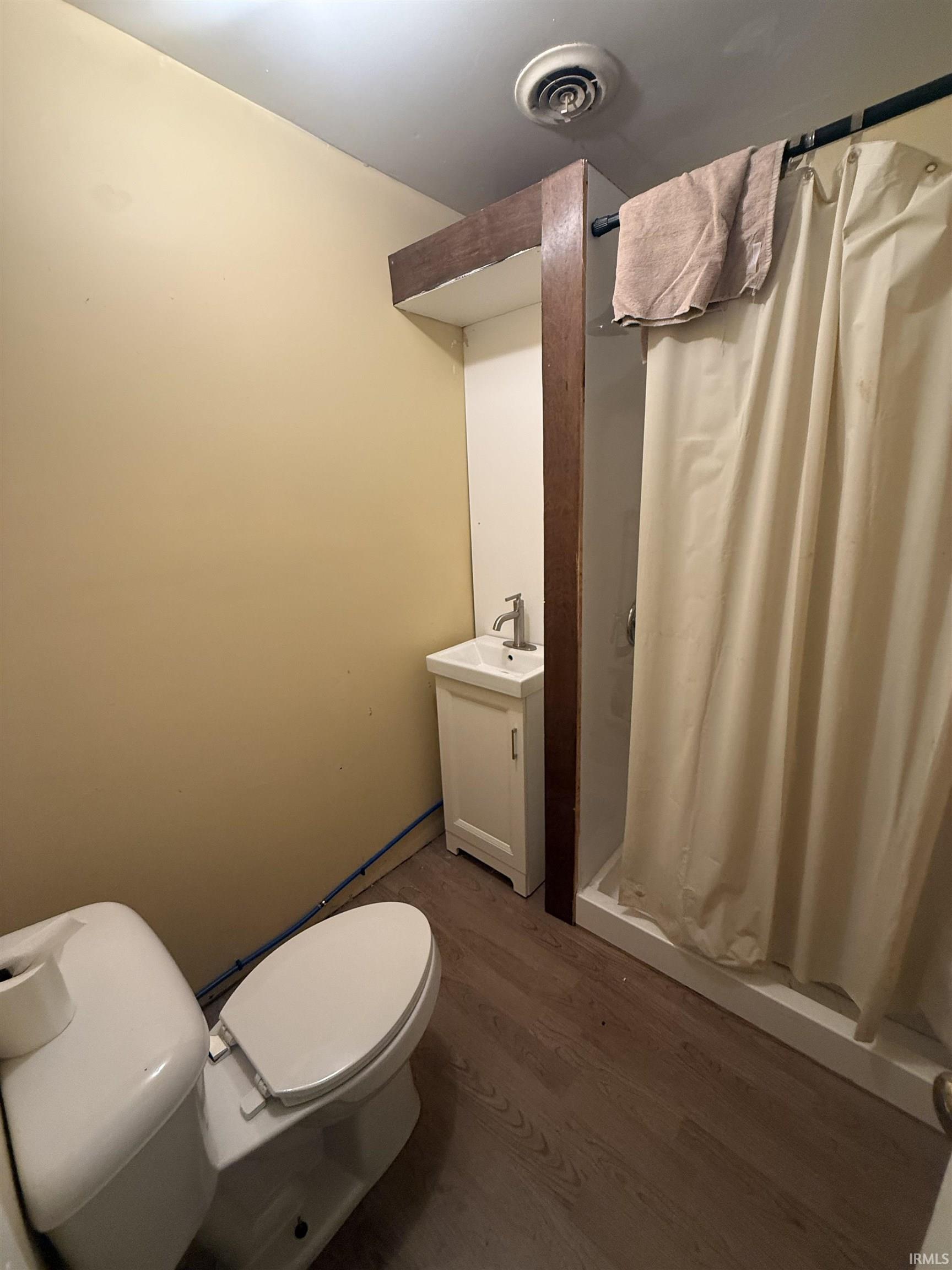 Compact bathroom featuring a white toilet, freestanding vanity with sink, and a shower with a shower curtain