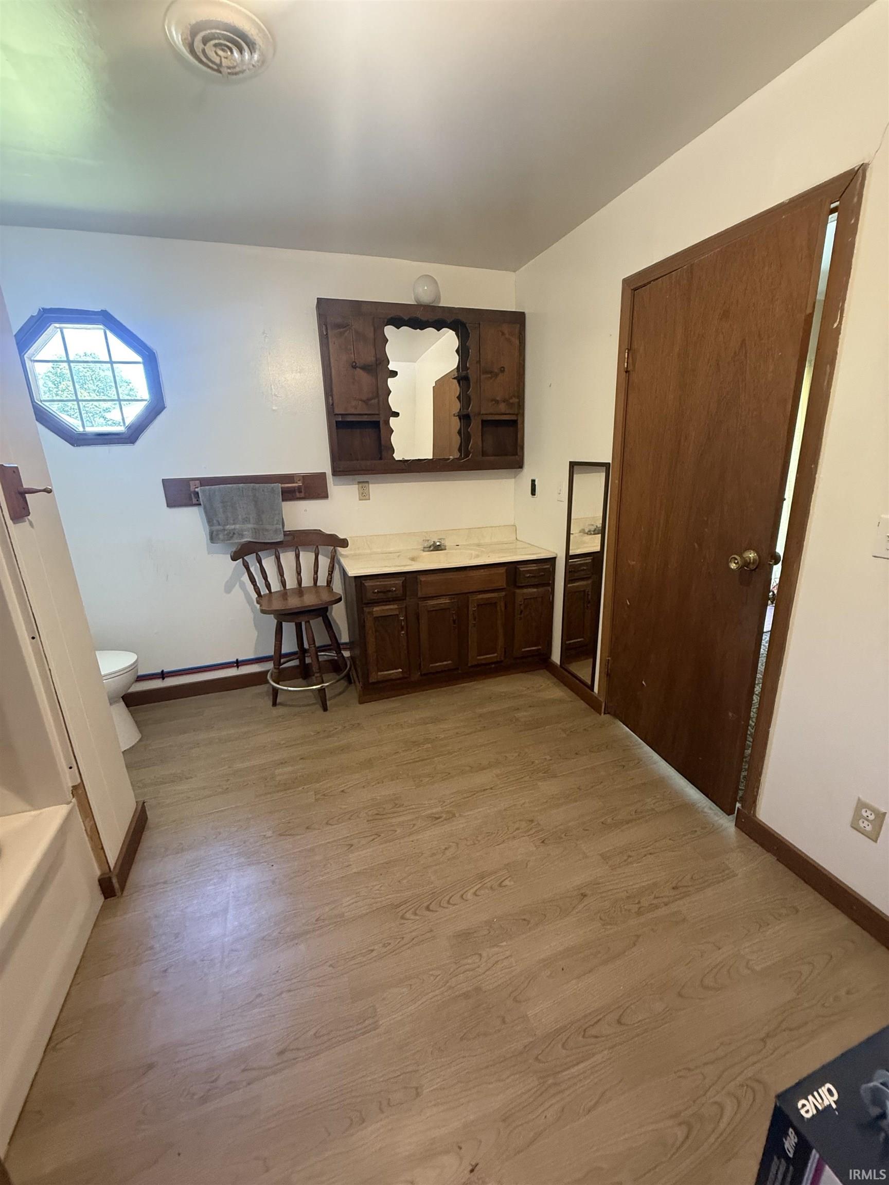 Bathroom featuring wood-finish flooring, a wood vanity with integrated sink, and an octagonal window