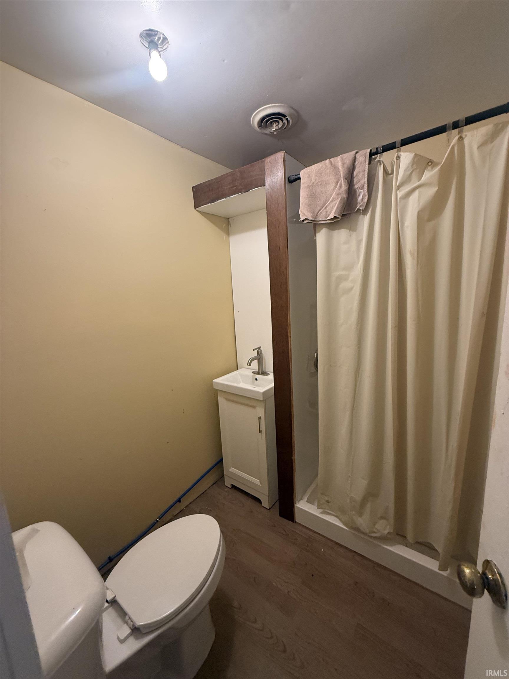 Bathroom featuring a white vanity with a single basin, a toilet, and wood-finish flooring