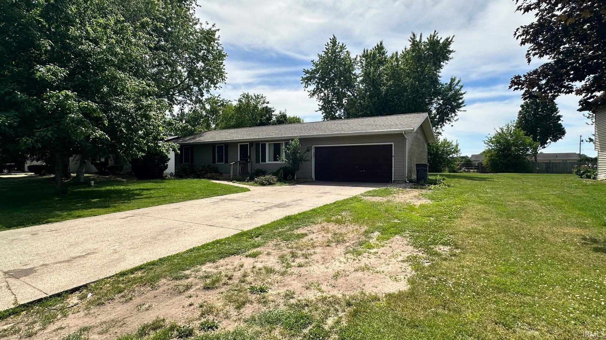 Ranch-style residence featuring a broad front lawn, integrated garage with a black door, concrete driveway, and mature landscaping