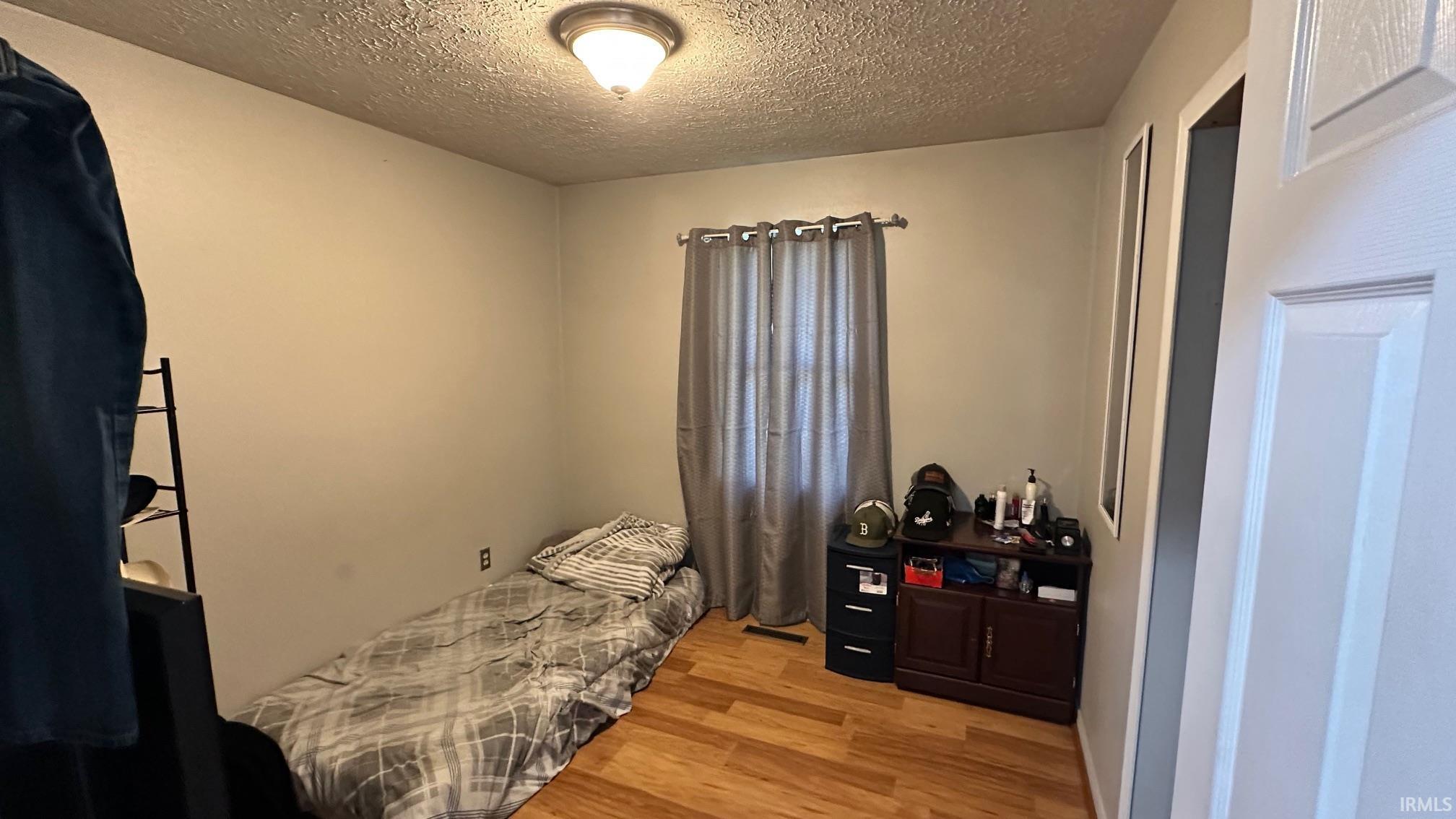 Wood-finish flooring with a window featuring privacy drapery