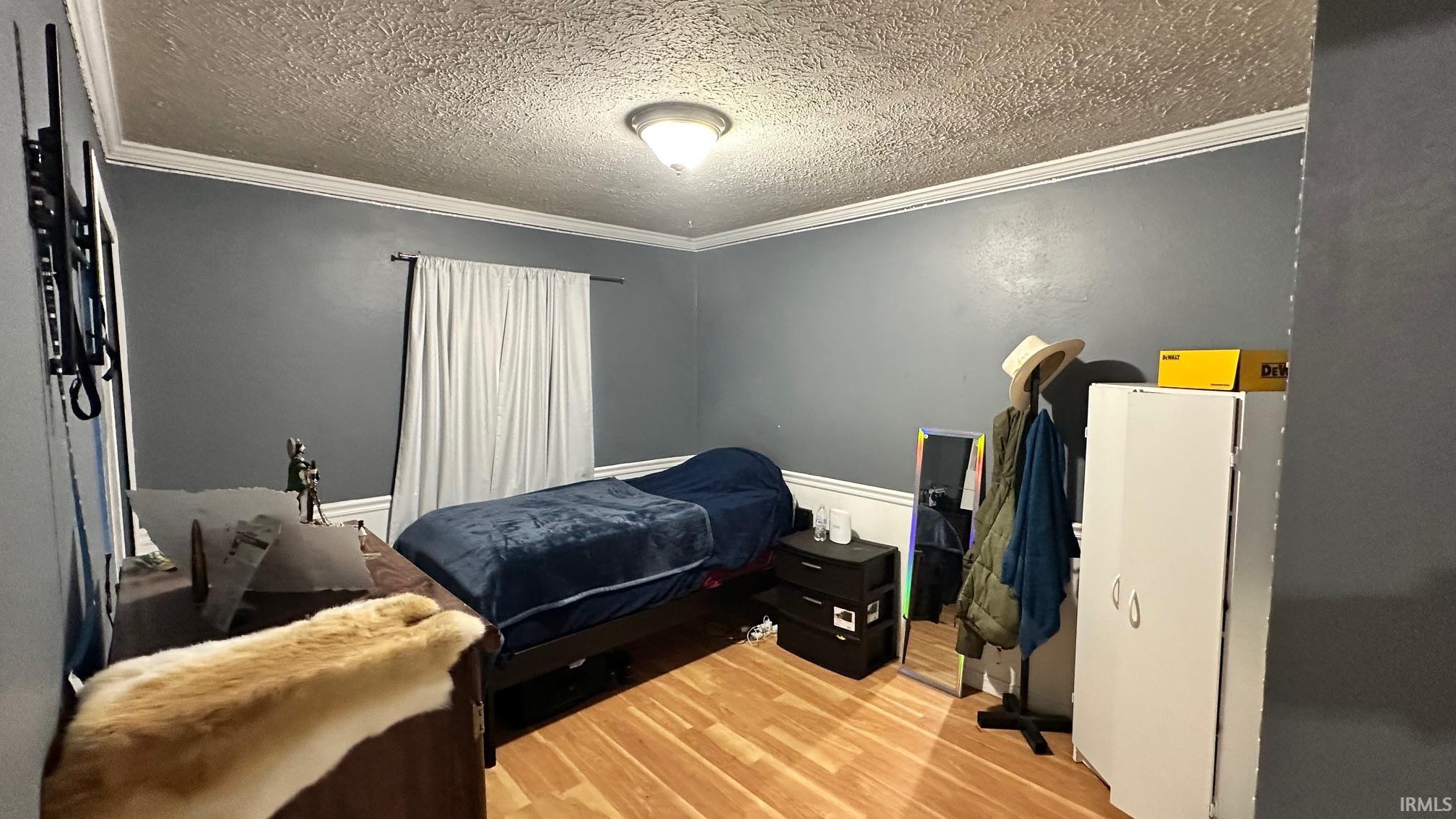 Room featuring wood-finish flooring, crown molding, and a neutral wall color