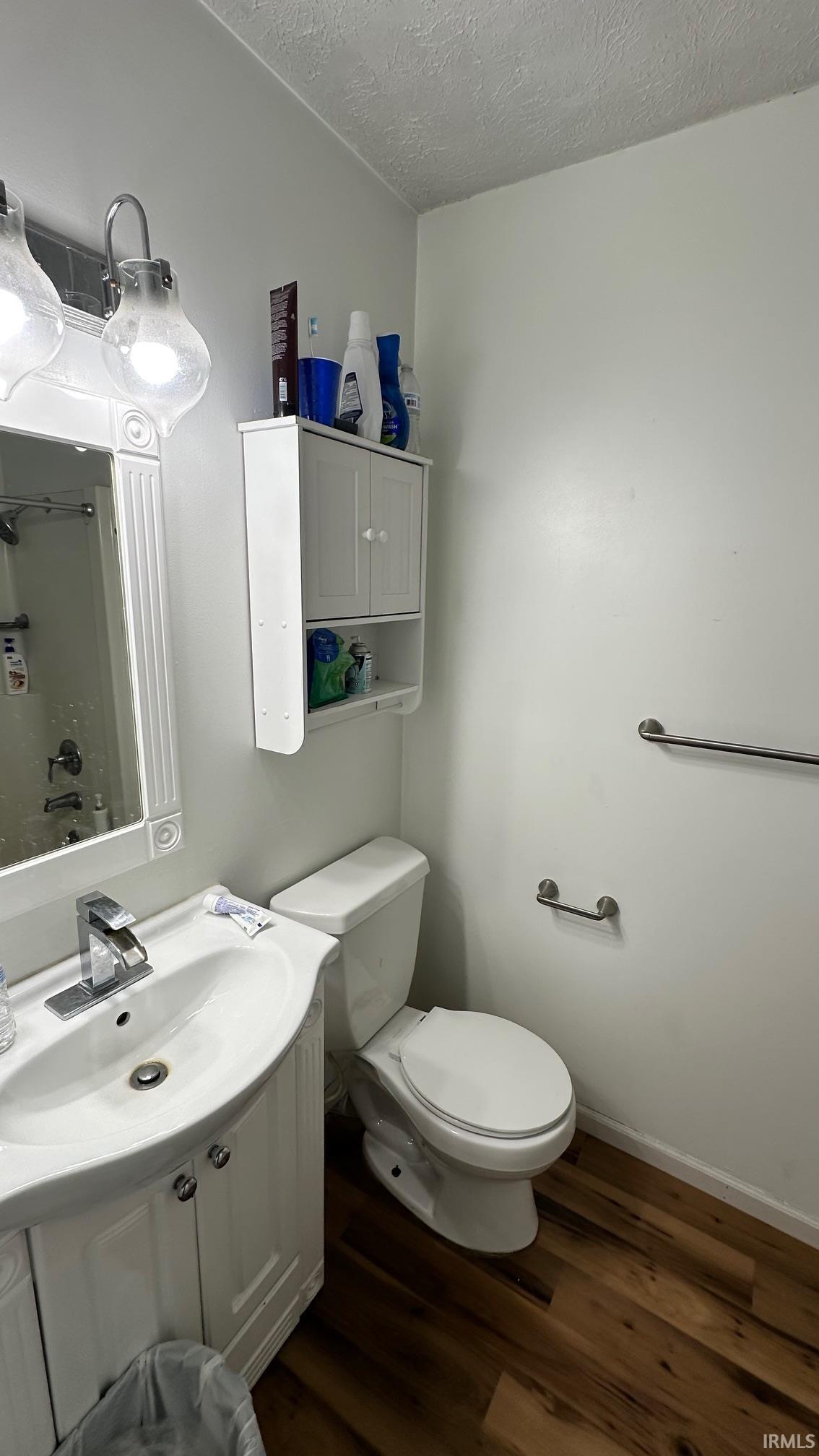 Bathroom featuring a white vanity with an integrated sink, a matching white toilet, wood-finish flooring, a wall-mounted medicine cabinet, and a framed mirror with overhead lighting