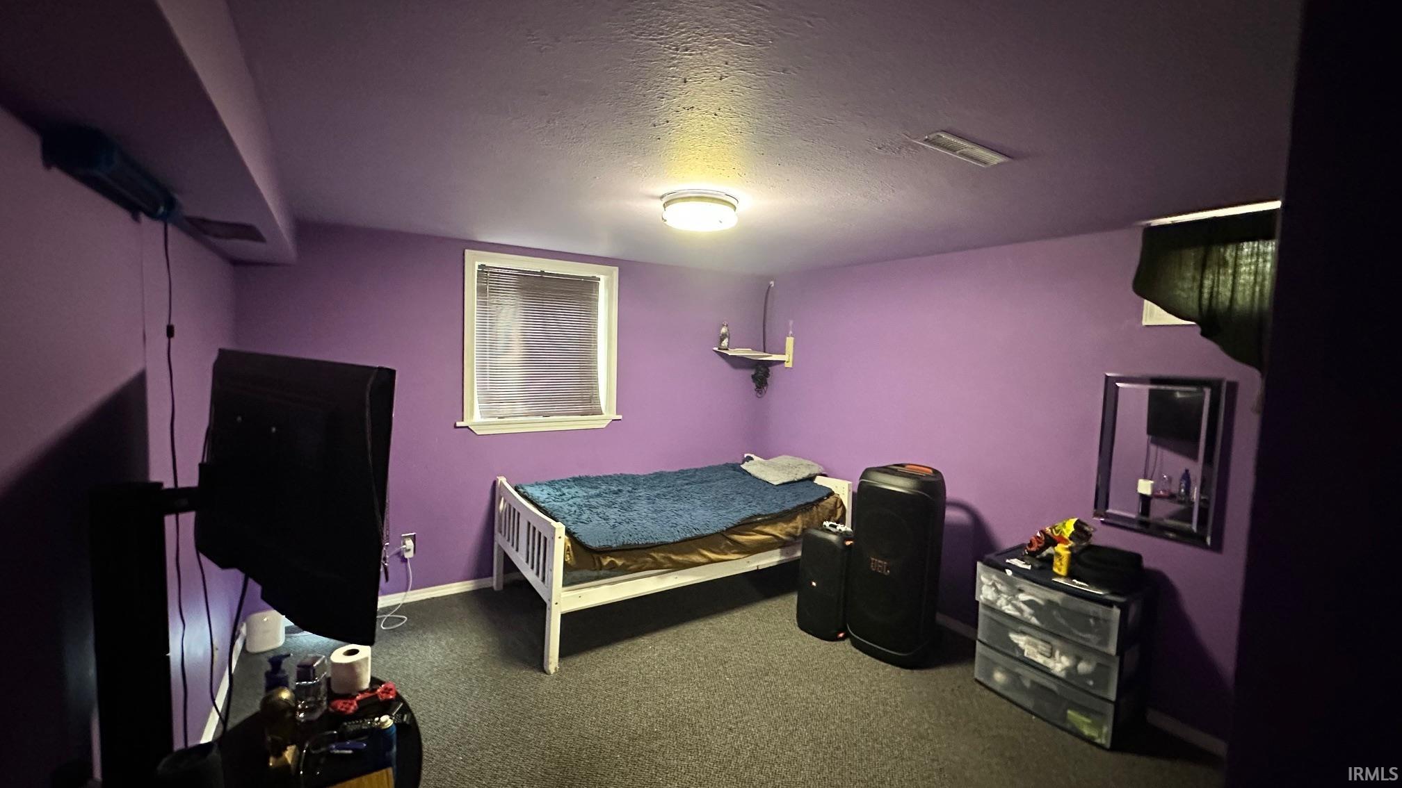 Carpeted interior space featuring a window with horizontal blinds, a wall-mounted shelf, and a ceiling-mounted light fixture